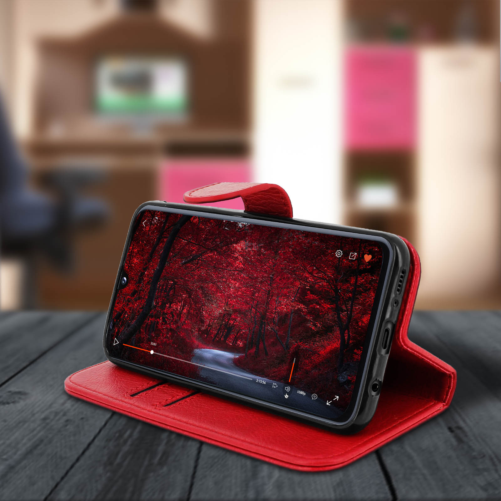 Étui de téléphone en cuir rouge avec un téléphone à l'intérieur. Le téléphone montre une vidéo de forêt. Table en bois.