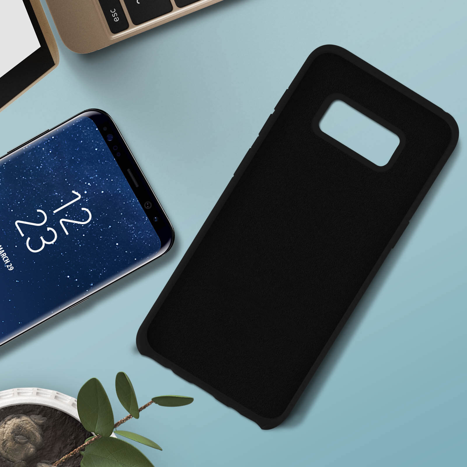 Telefono e custodia neri su superficie blu. Tastiera e pianta visibili.