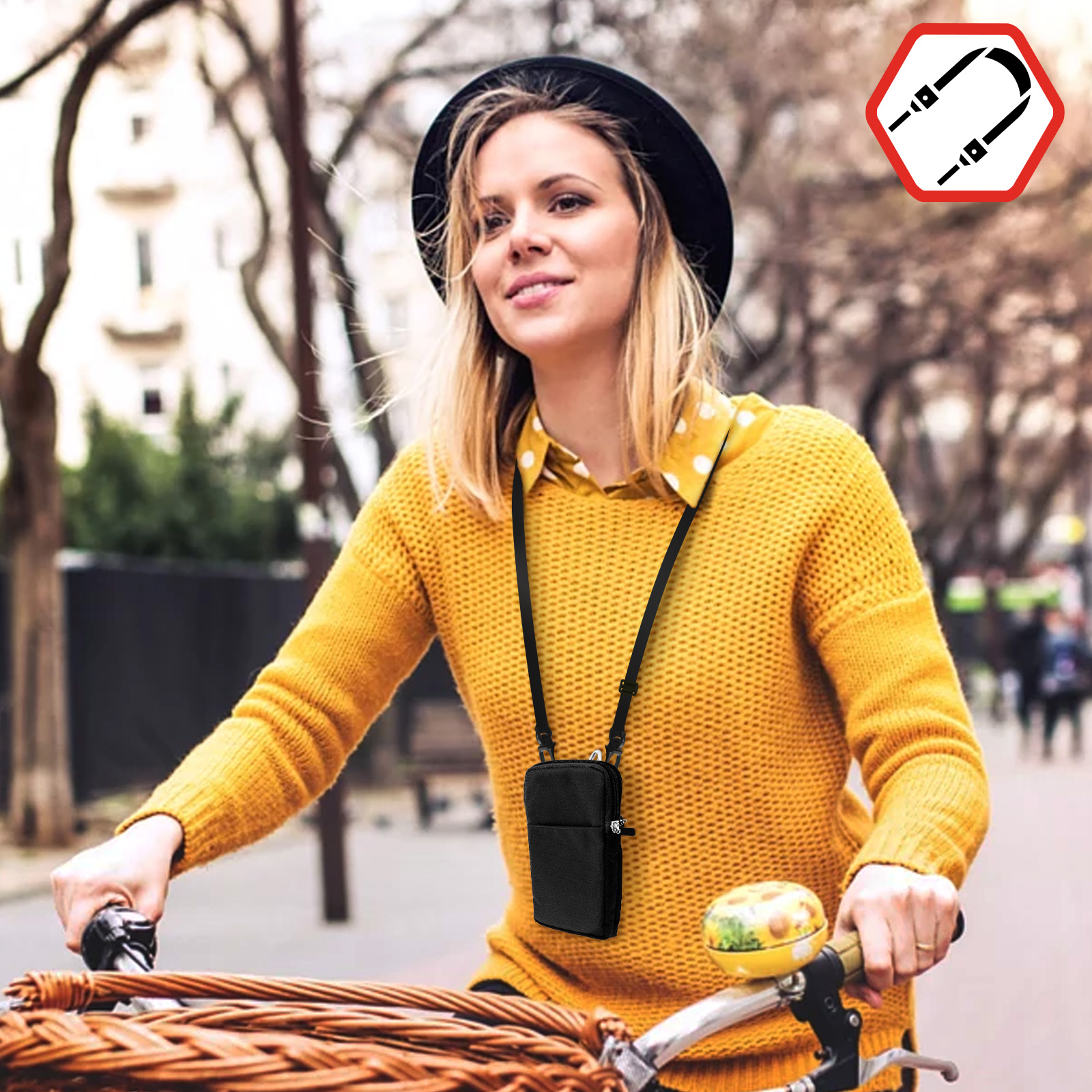Donna in bicicletta con maglione giallo e cappello nero, tiene custodia per telefono con tracolla.