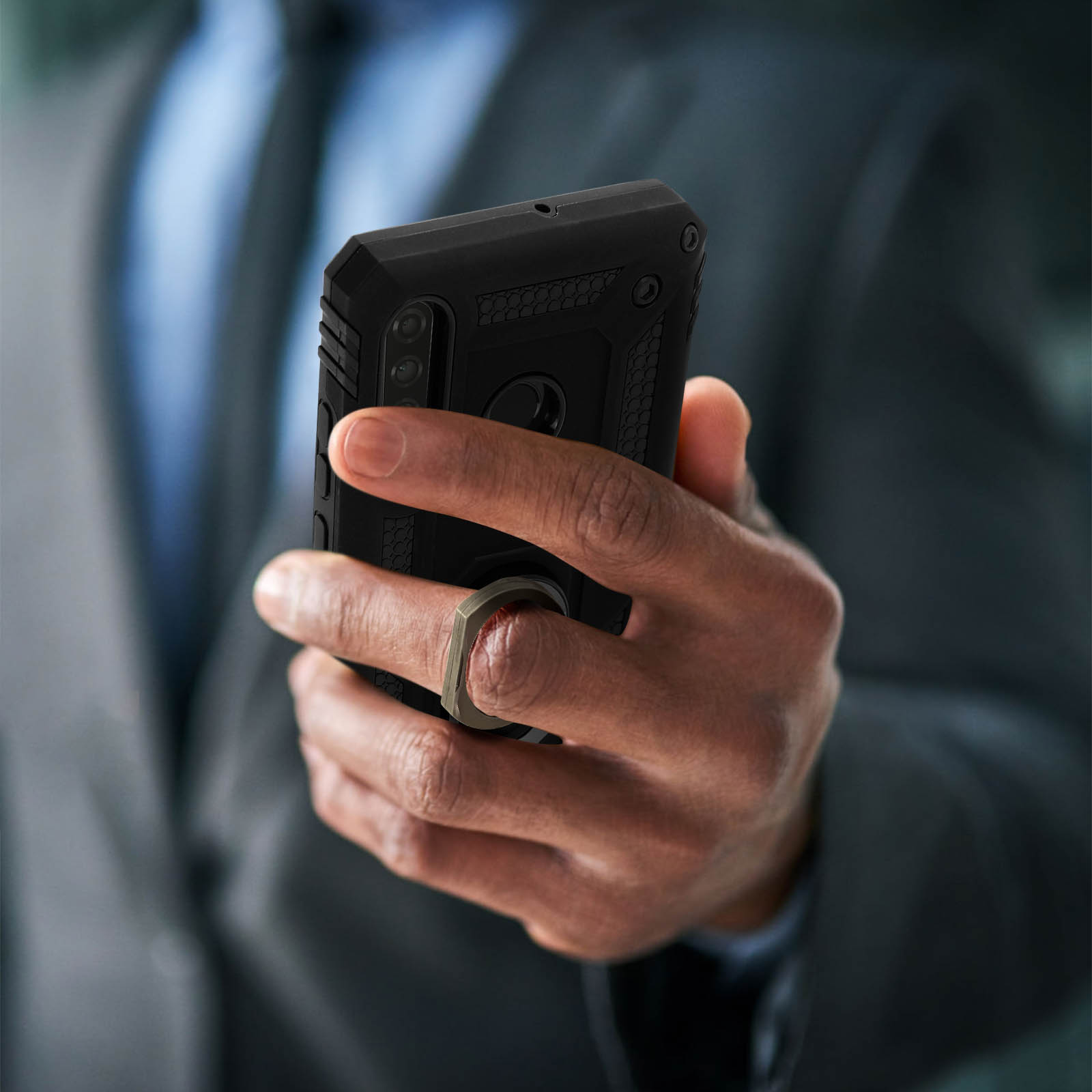 Een persoon die een zwarte telefoonhoes met een ringhouder vasthoudt. De persoon draagt een pak.