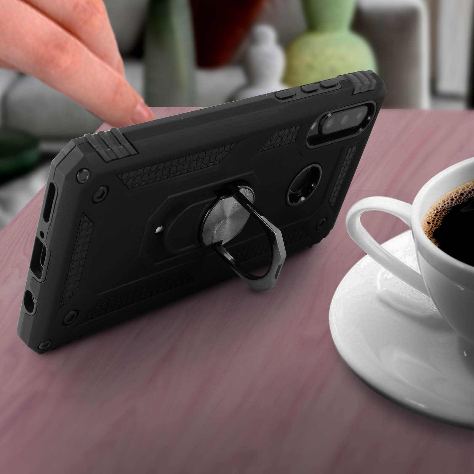 Zwarte telefoonhoes met een ringhouder. Een kopje koffie op de achtergrond.