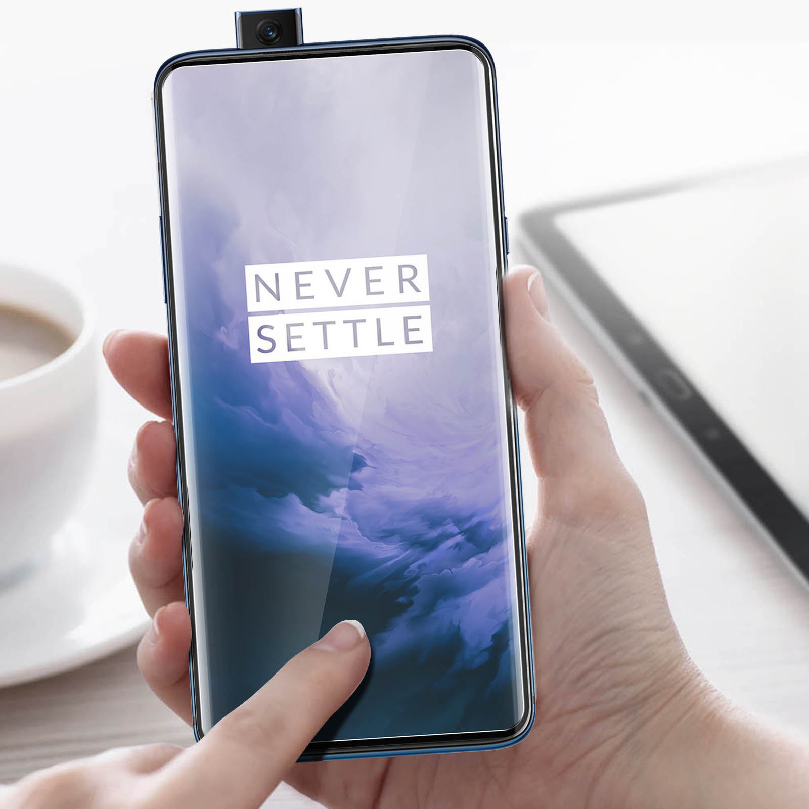 Une main tenant un téléphone avec le texte 'NEVER SETTLE' sur l'écran. Caméra pop-up visible.