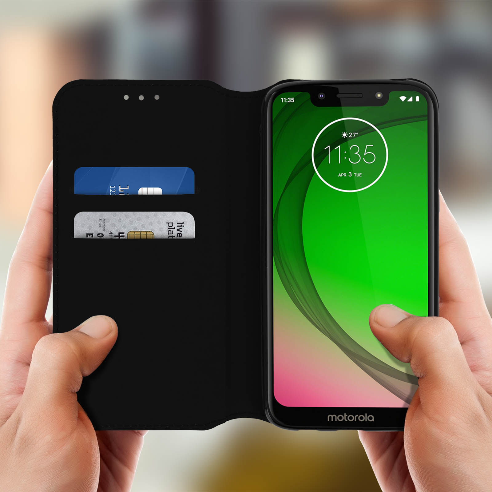 Handen houden een telefoon in een hoesje vast. De telefoon toont tijd en datum, en heeft kaarten.