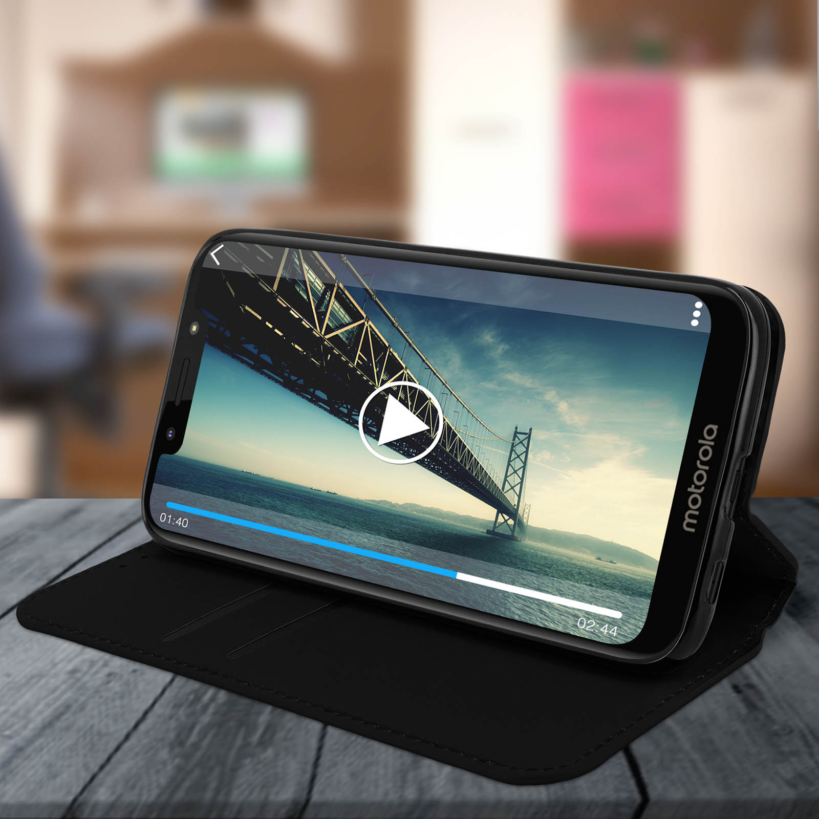 Zwarte telefoon in een hoesje, video afspelen. De achtergrond toont een brug en water.