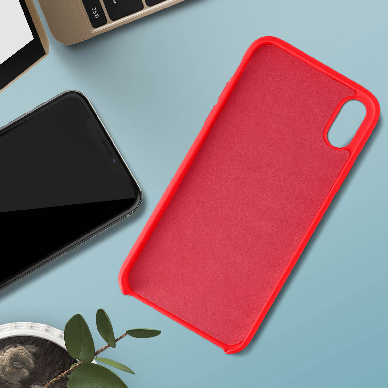 Una custodia rossa e un telefono nero sono accanto a un laptop e una pianta.