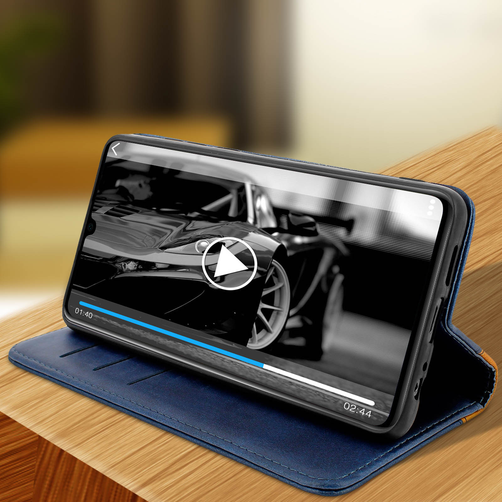 Telefono in custodia blu mostra video di auto. Tavolo in legno e sfondo sfocato.