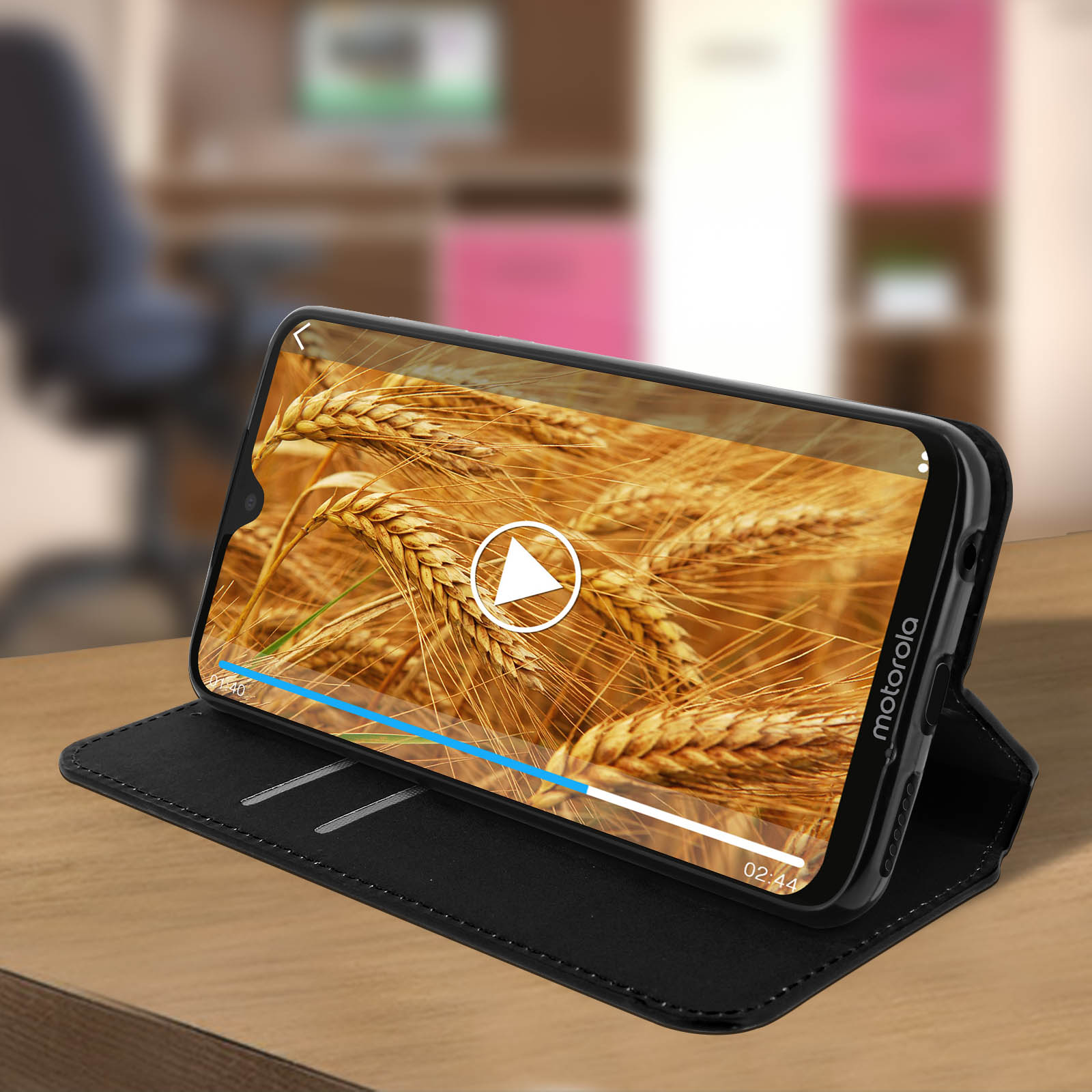 Un telefono in una custodia nera è in un supporto, che riproduce un video di campi di grano.