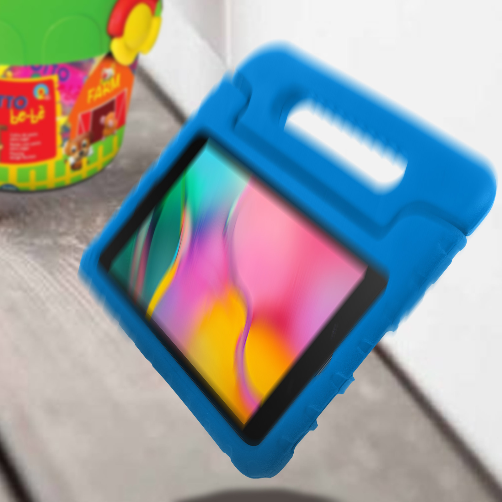 Blaues Tablet in blauem Schaumstoffetui. Grüner und gelber Spielzeugeimer im Hintergrund.