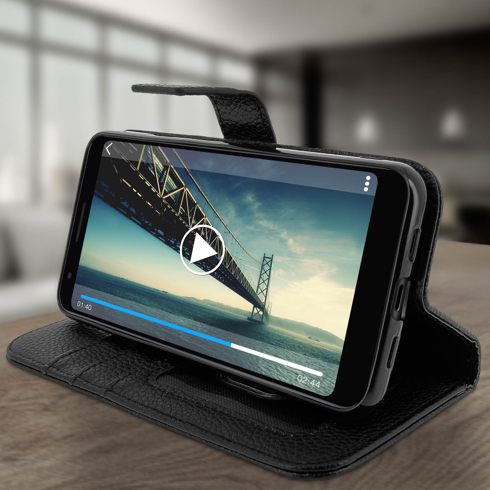 Telefono in custodia di pelle nera che mostra un video di un ponte. È su un tavolo di legno.