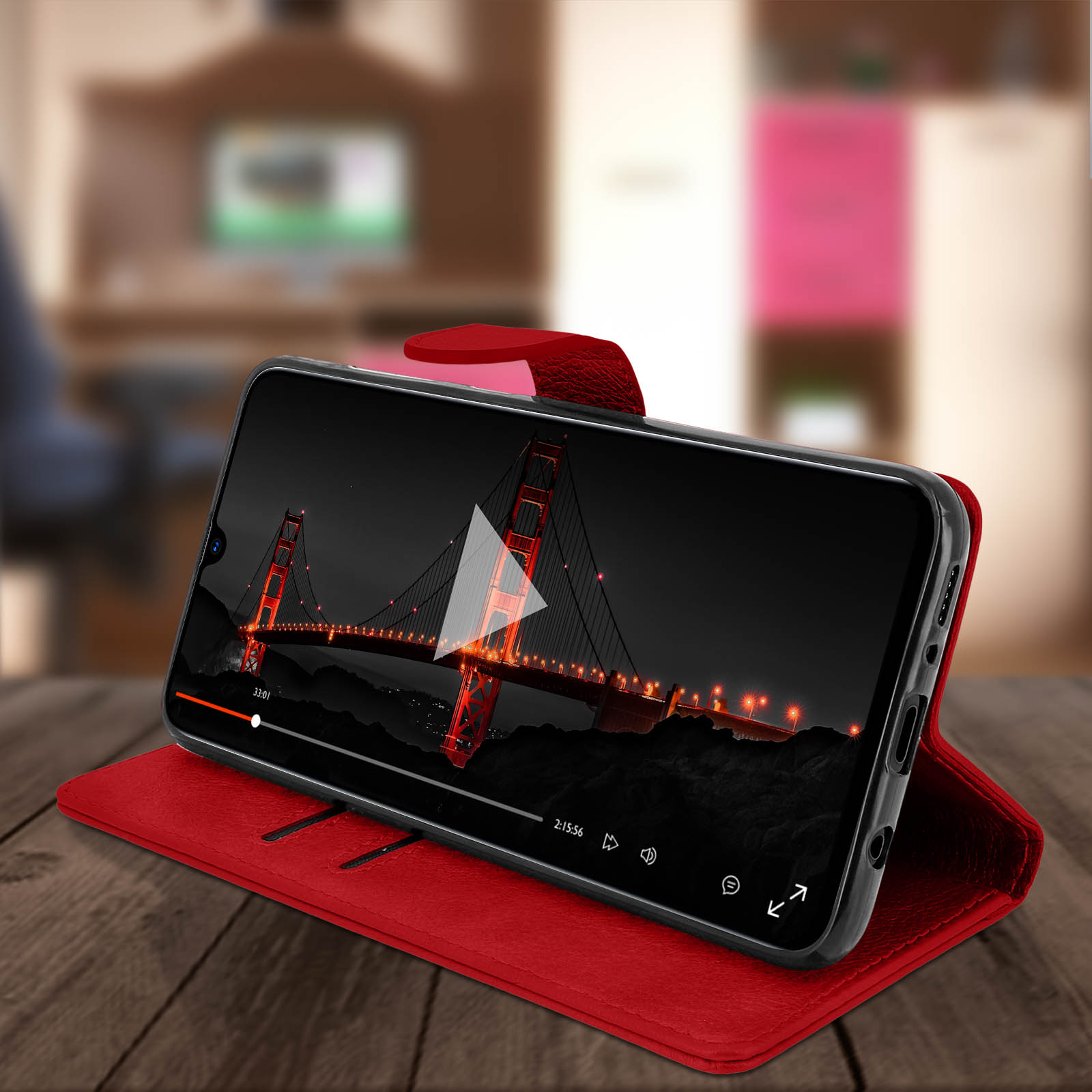 Een telefoon in een rode hoes toont een video van de Golden Gate Bridge, op een houten tafel.