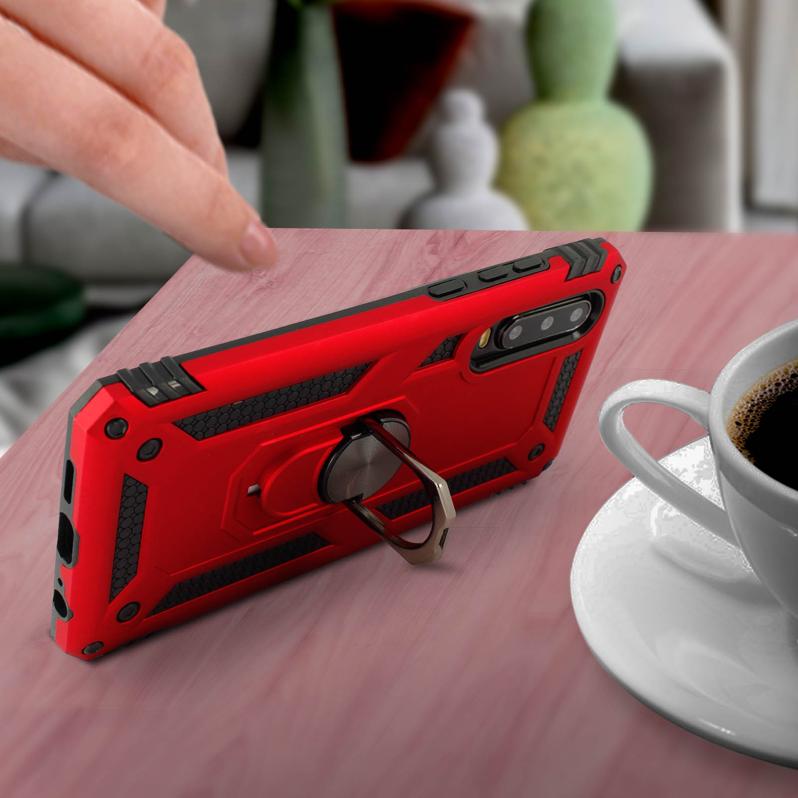 Rode telefoonhoes met ringhouder op een houten tafel, en een witte kop koffie ernaast.