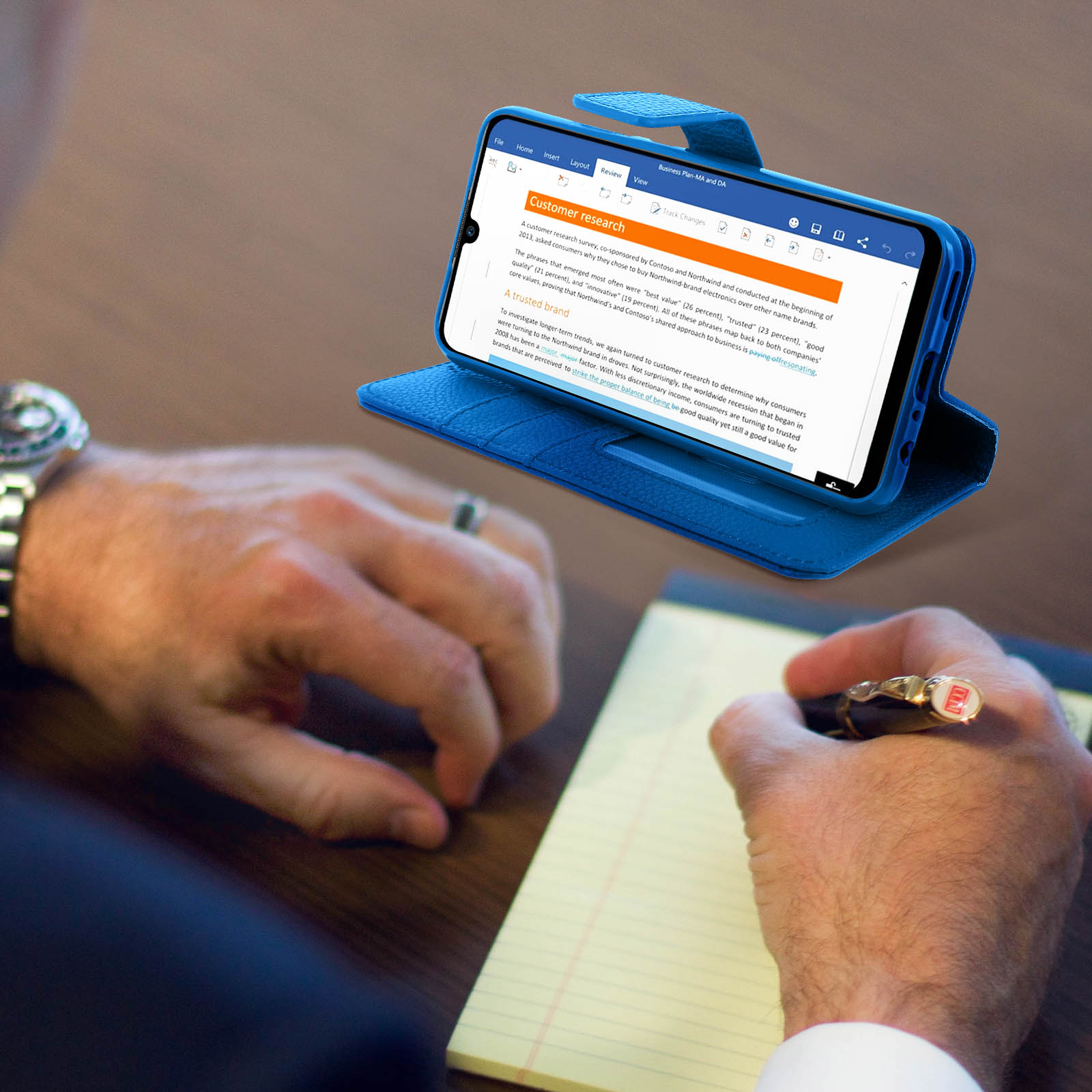 Téléphone dans un étui bleu, ouvert, avec un document à l'écran. Une personne écrit.