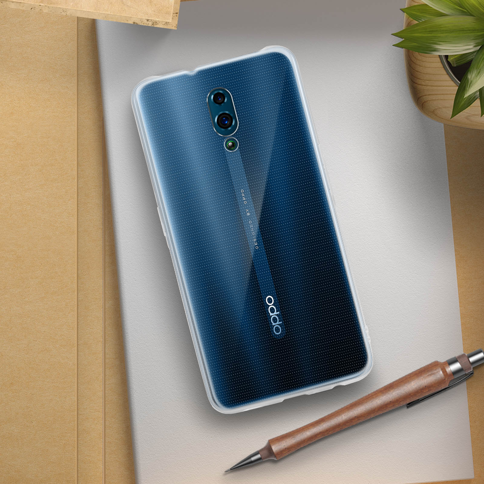 Ein Telefon mit transparentem Gehäuse liegt auf einer Oberfläche. Ein Stift und eine Pflanze befinden sich ebenfalls auf der Oberfläche.