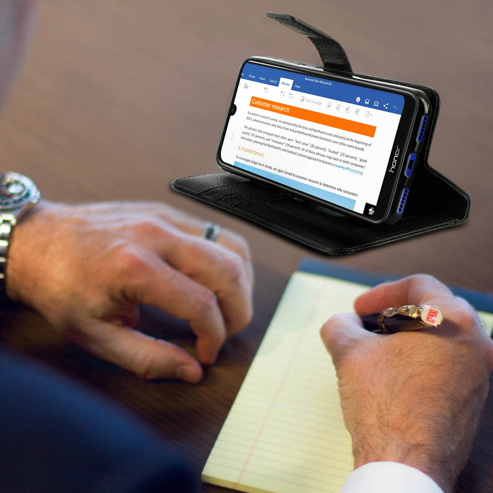 Un uomo scrive su un blocco note con un telefono che mostra la ricerca sui clienti.