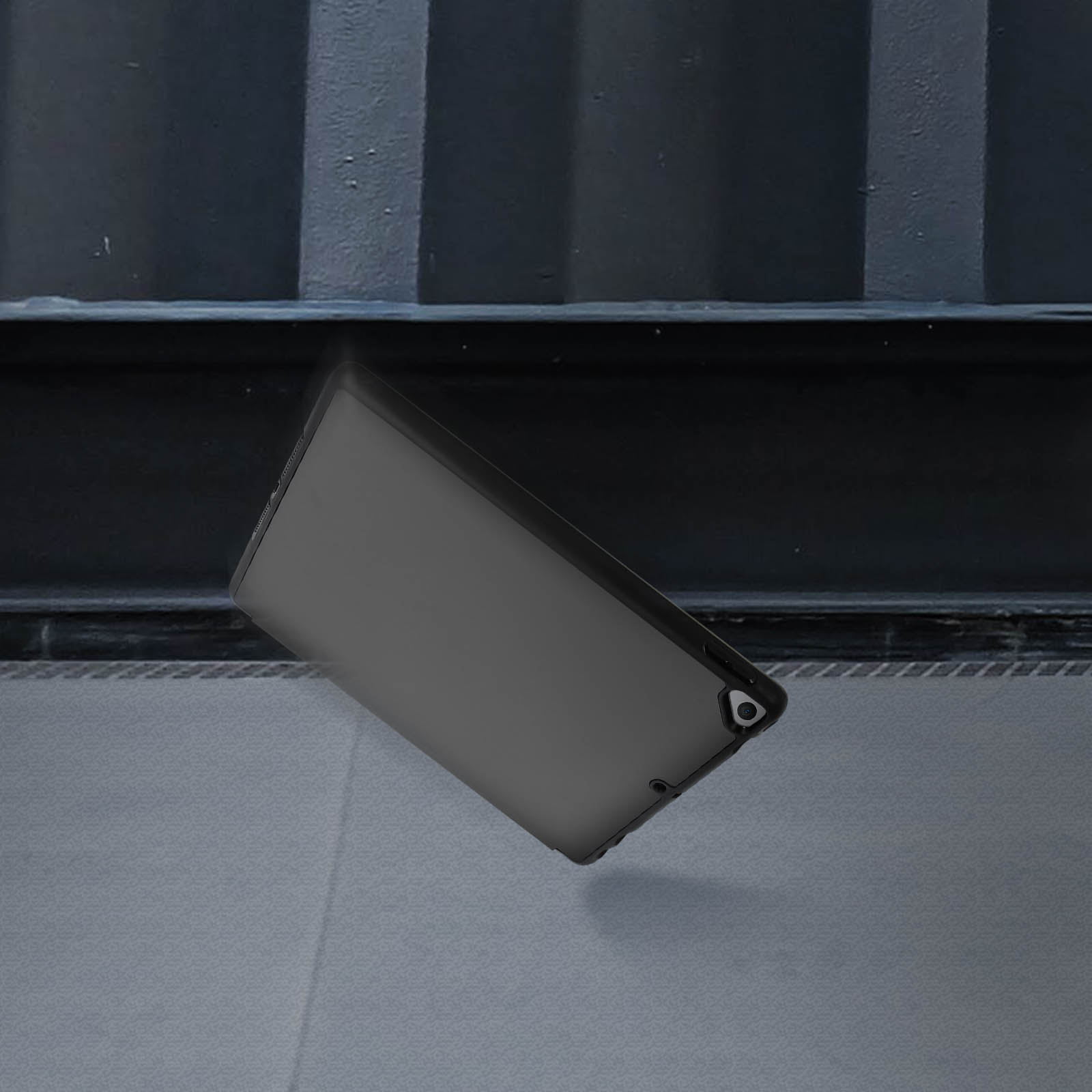 Tablet nero che cade. Sfondo scuro, forse un container o una porta.