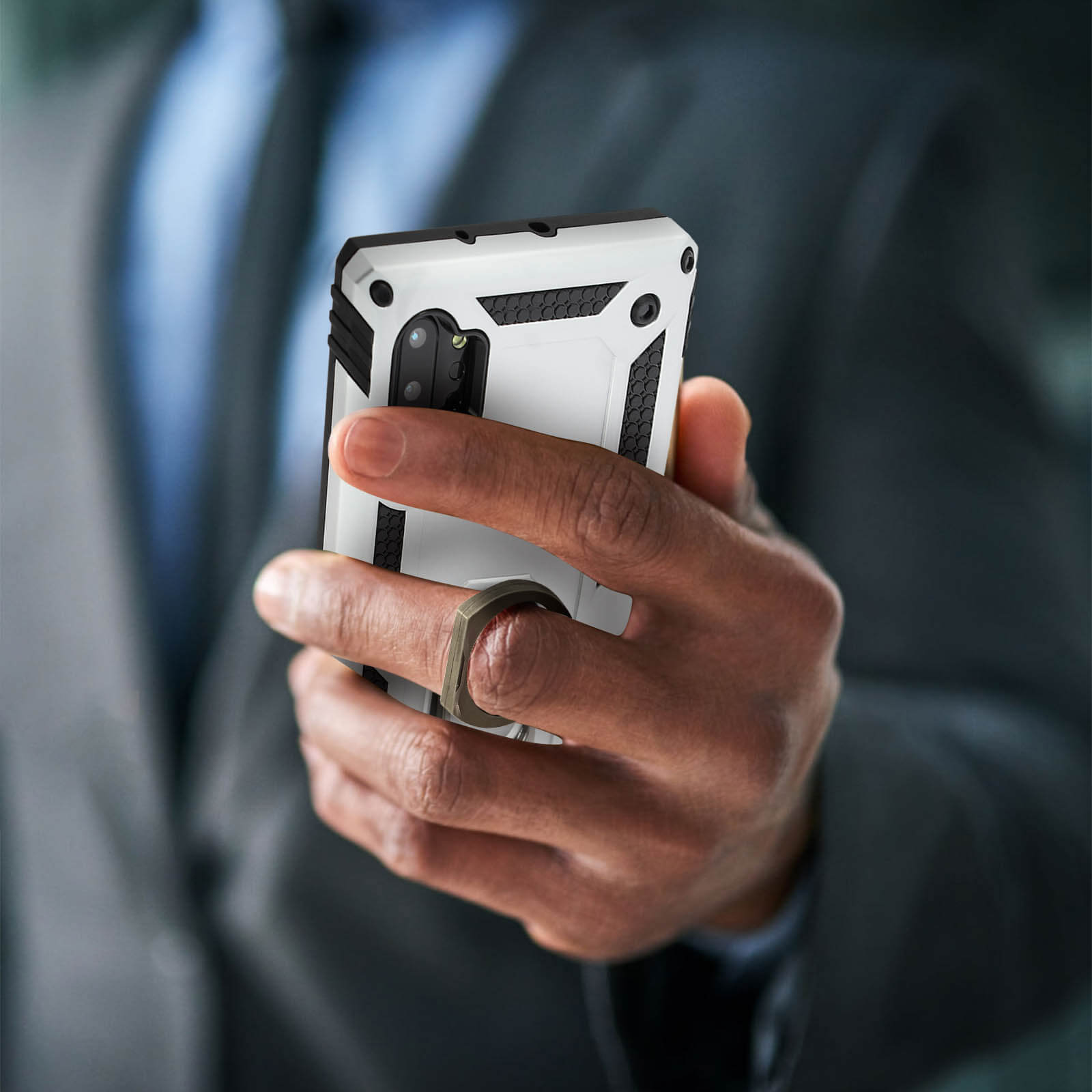 Une main tenant une coque de téléphone blanche. La coque a un support de bague. Fond sombre.
