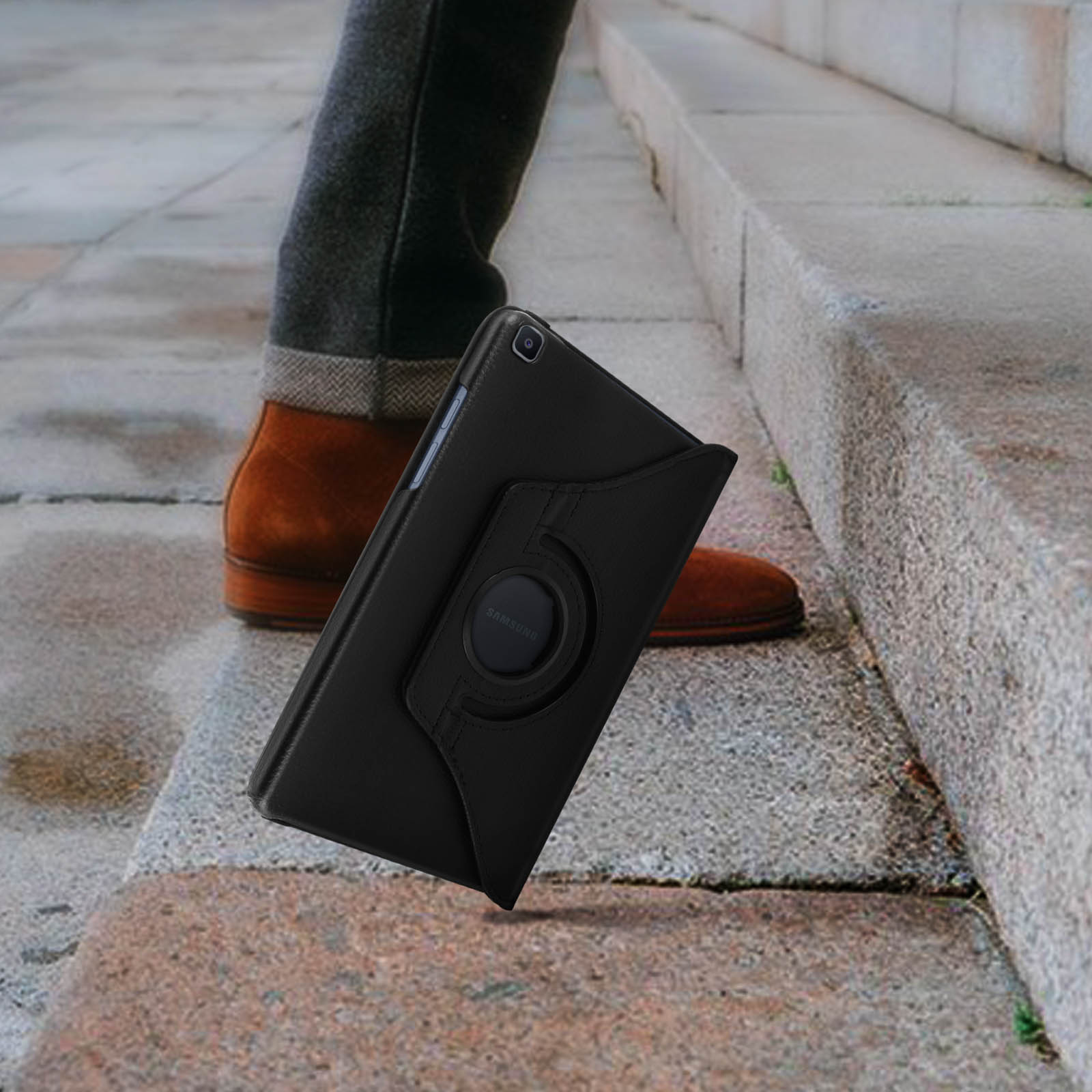 Custodia nera per tablet sui gradini. Gambe di una persona e scarpe marroni sullo sfondo.