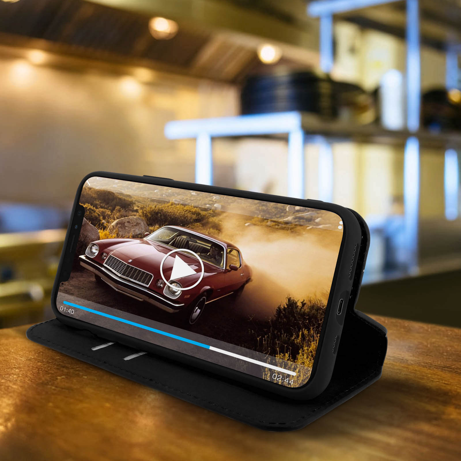 Un téléphone dans un étui portefeuille noir affiche une vidéo d'une voiture rouge sur une table en bois.