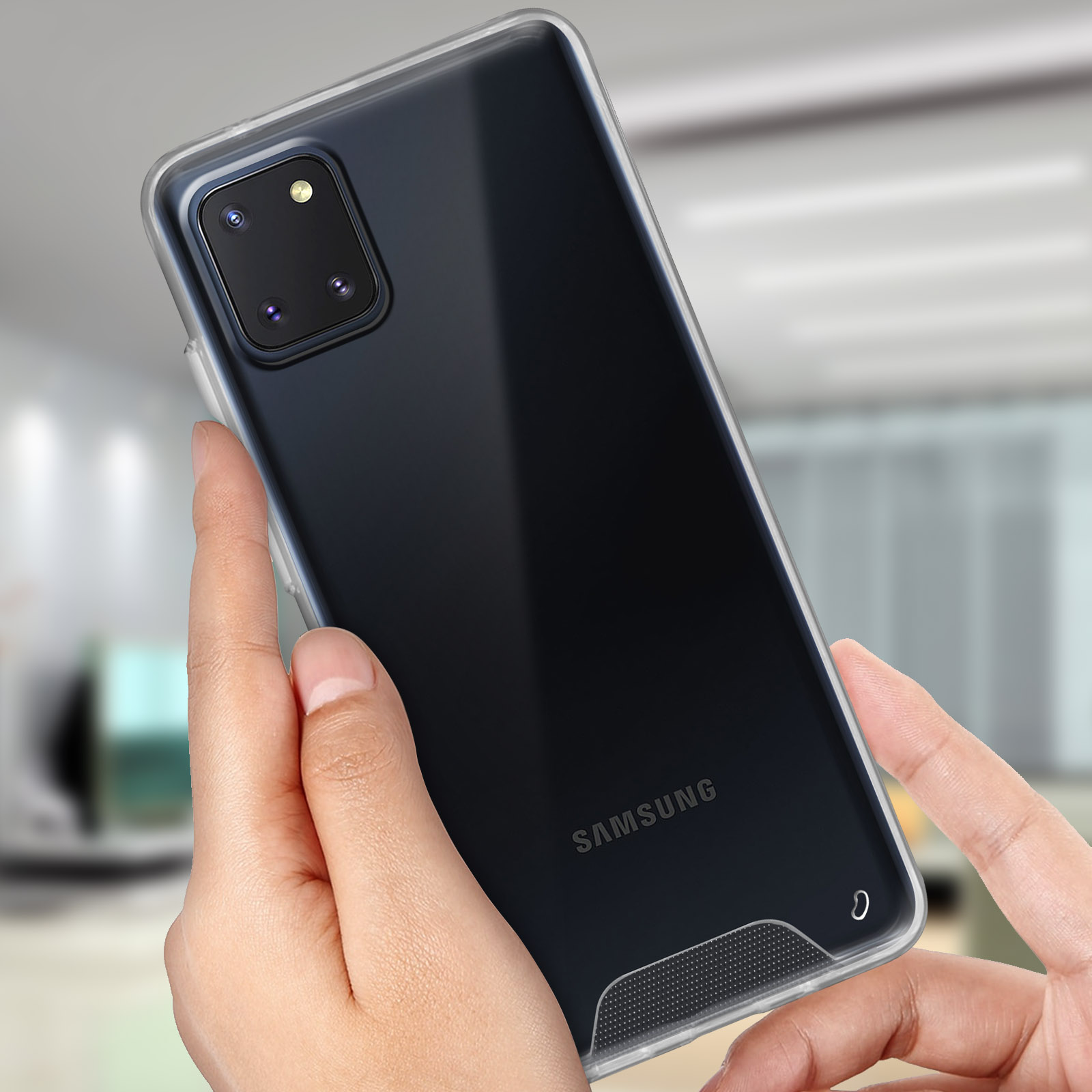 Una mano tiene un telefono in una custodia trasparente. Il telefono mostra il logo Samsung. Lo sfondo è sfocato.