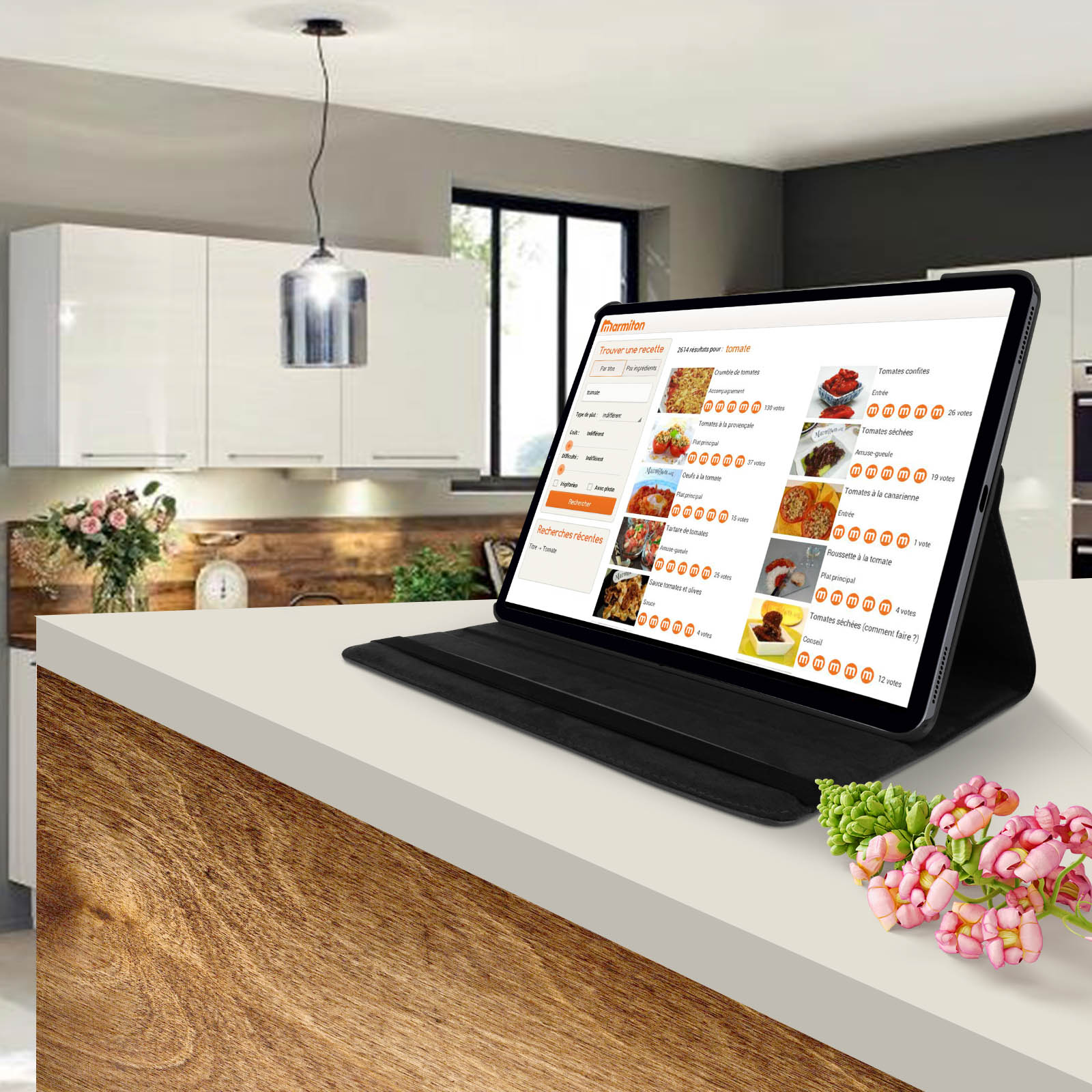 Tablet su un bancone della cucina che mostra un sito web di ricette. Fiori in primo piano. Cucina sullo sfondo.