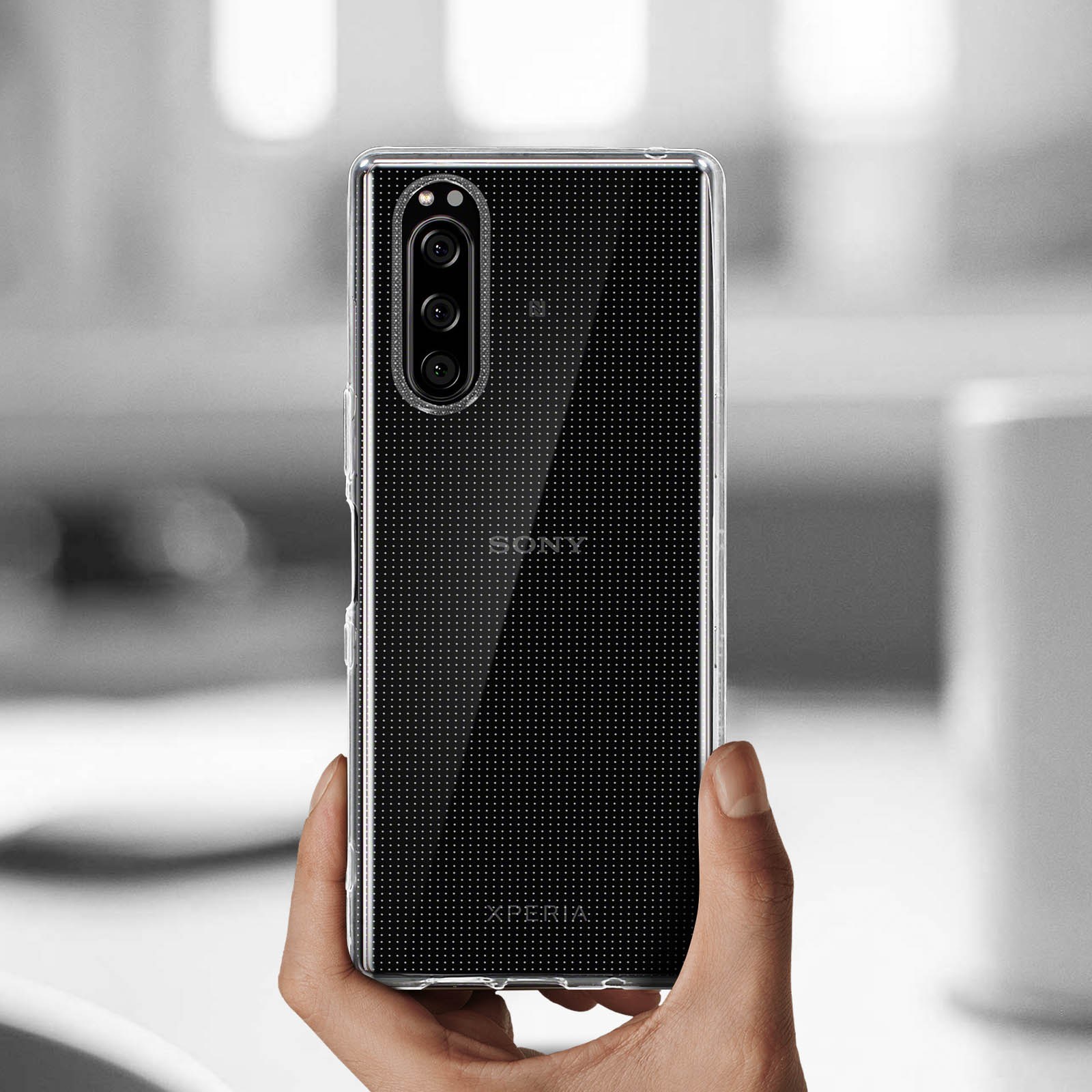 Une main tenant une coque de téléphone transparente. Motif à pois sur la coque.