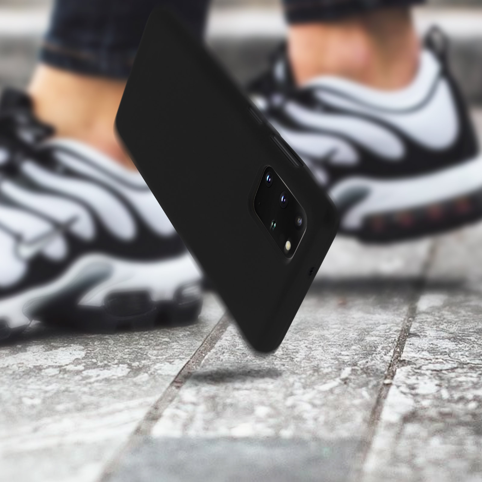 Coque de téléphone noire tombant, avec des baskets en arrière-plan.