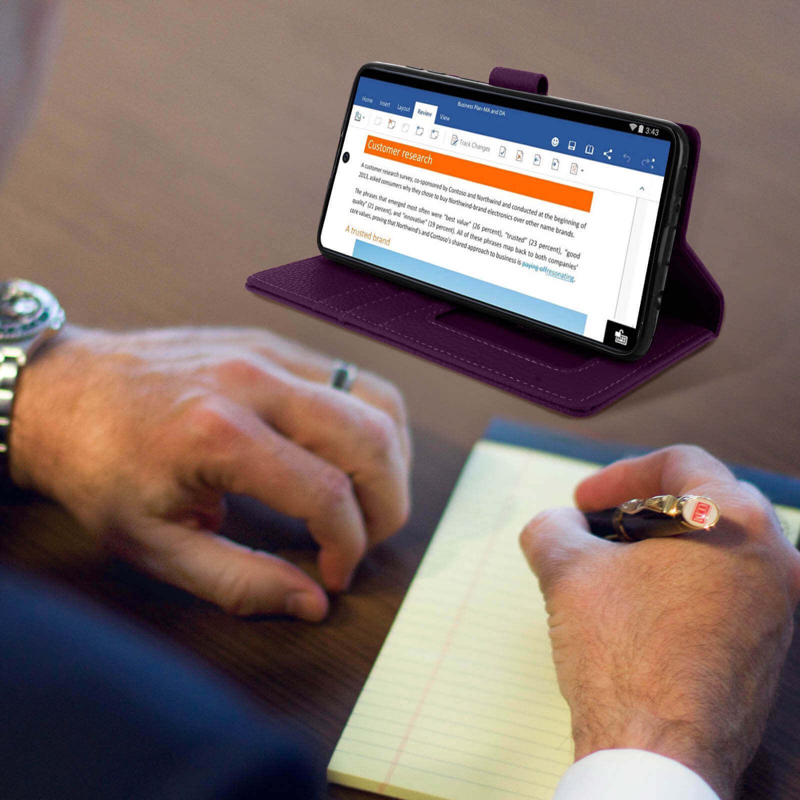 Téléphone dans un étui violet avec un document à l'écran. Une personne écrit avec un stylo.