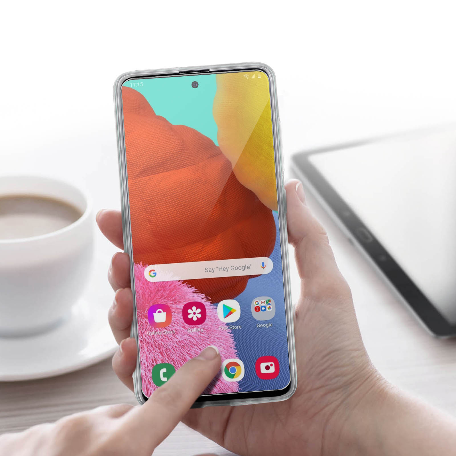 Una mano che tiene un telefono che mostra una schermata dell'app, con una tazza di caffè e un tablet sullo sfondo.