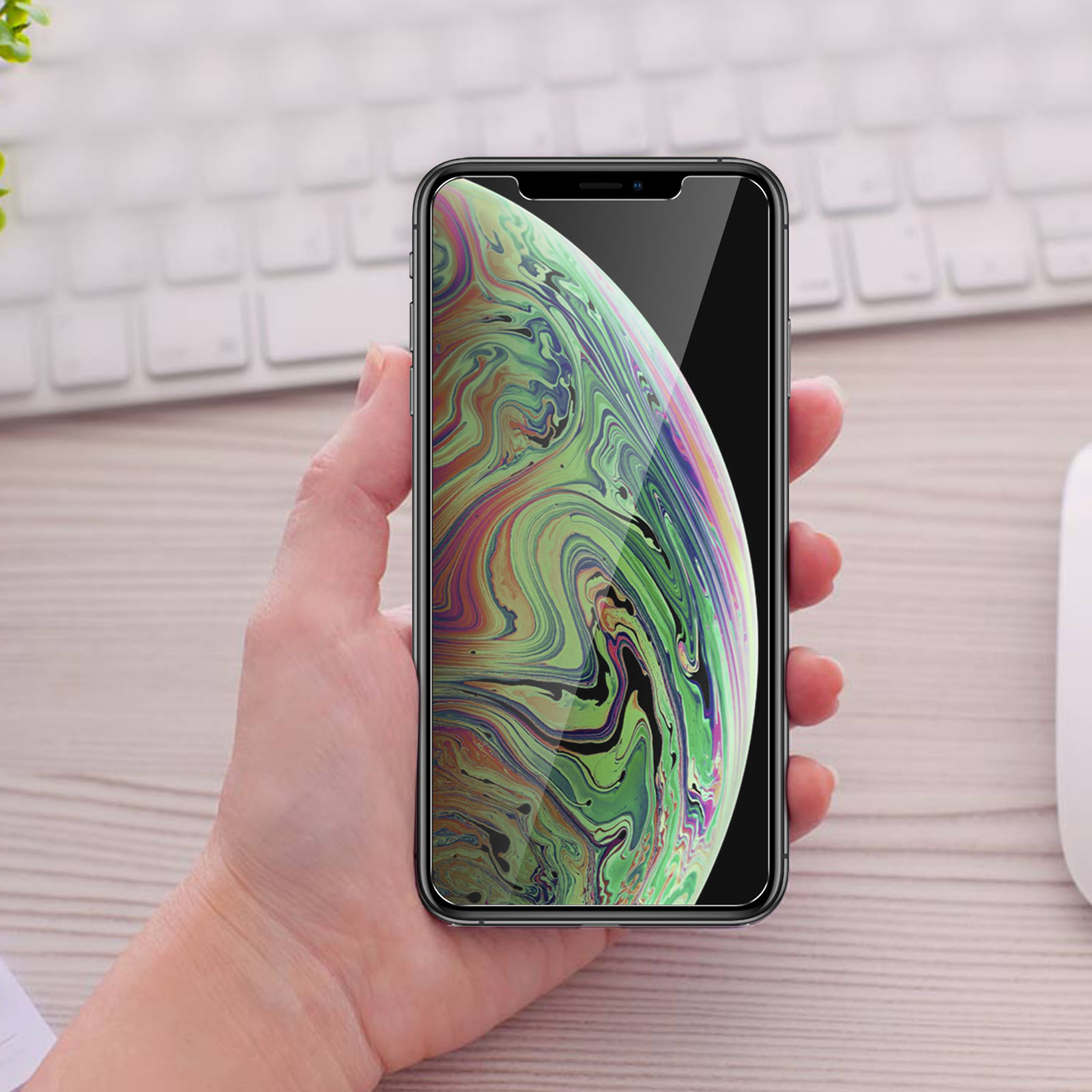 Telefono con protezione schermo, in mano. Sfondo: tastiera e mouse.
