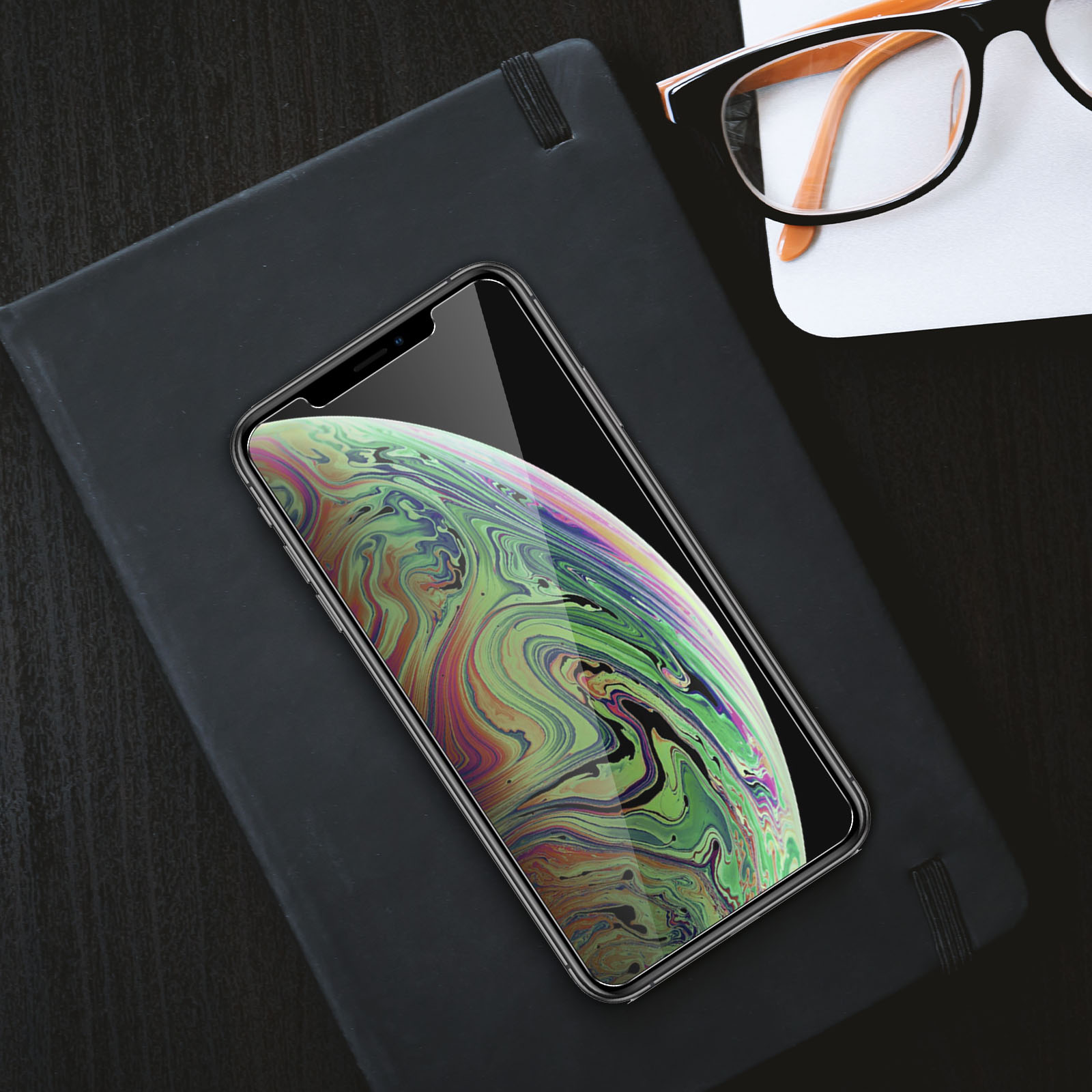 Un telefono in una custodia su un blocco note con occhiali. Il telefono mostra un'immagine planetaria.
