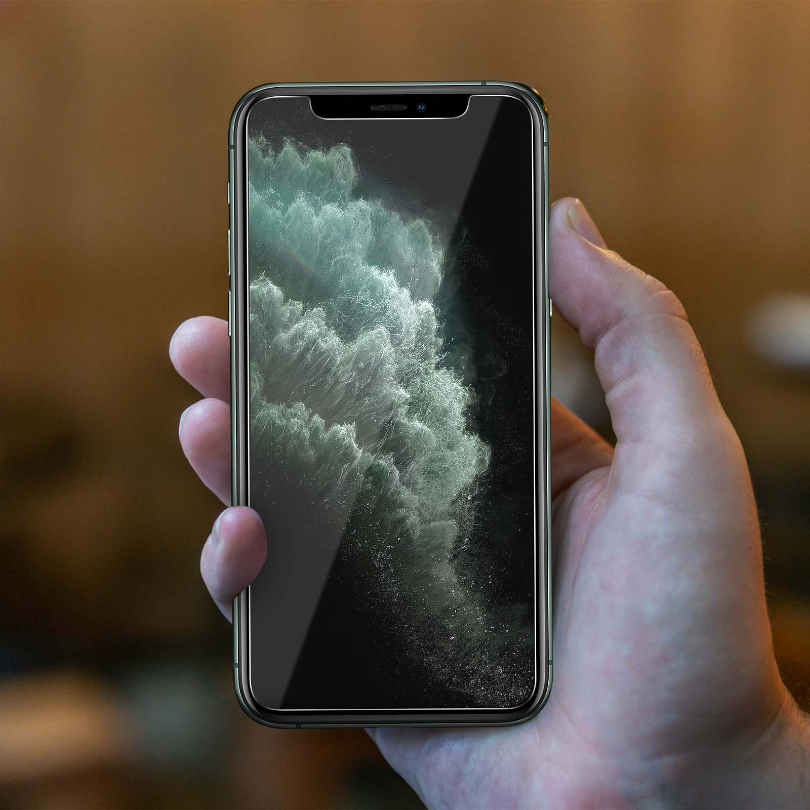 Hand holding a phone with a clear screen, with a blurry background visible.