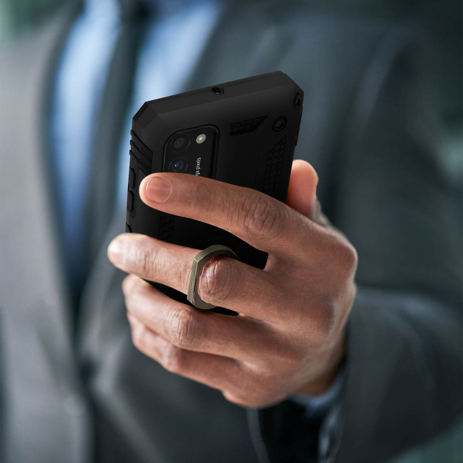 Mano che tiene un telefono nero con supporto ad anello. Persona in giacca e cravatta. Sfondo sfocato.