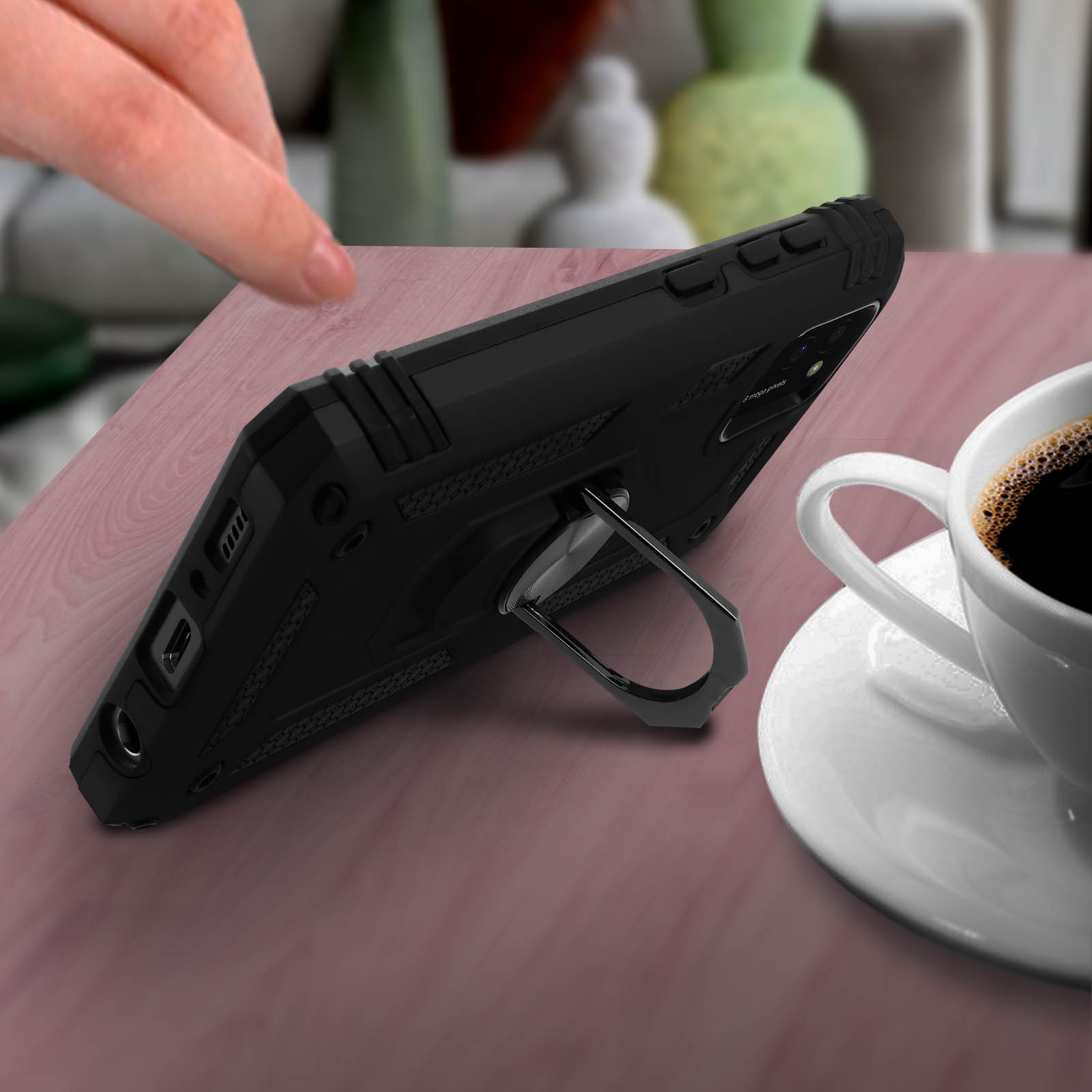 Custodia per telefono nera con supporto ad anello su un tavolo di legno accanto a una tazza di caffè.