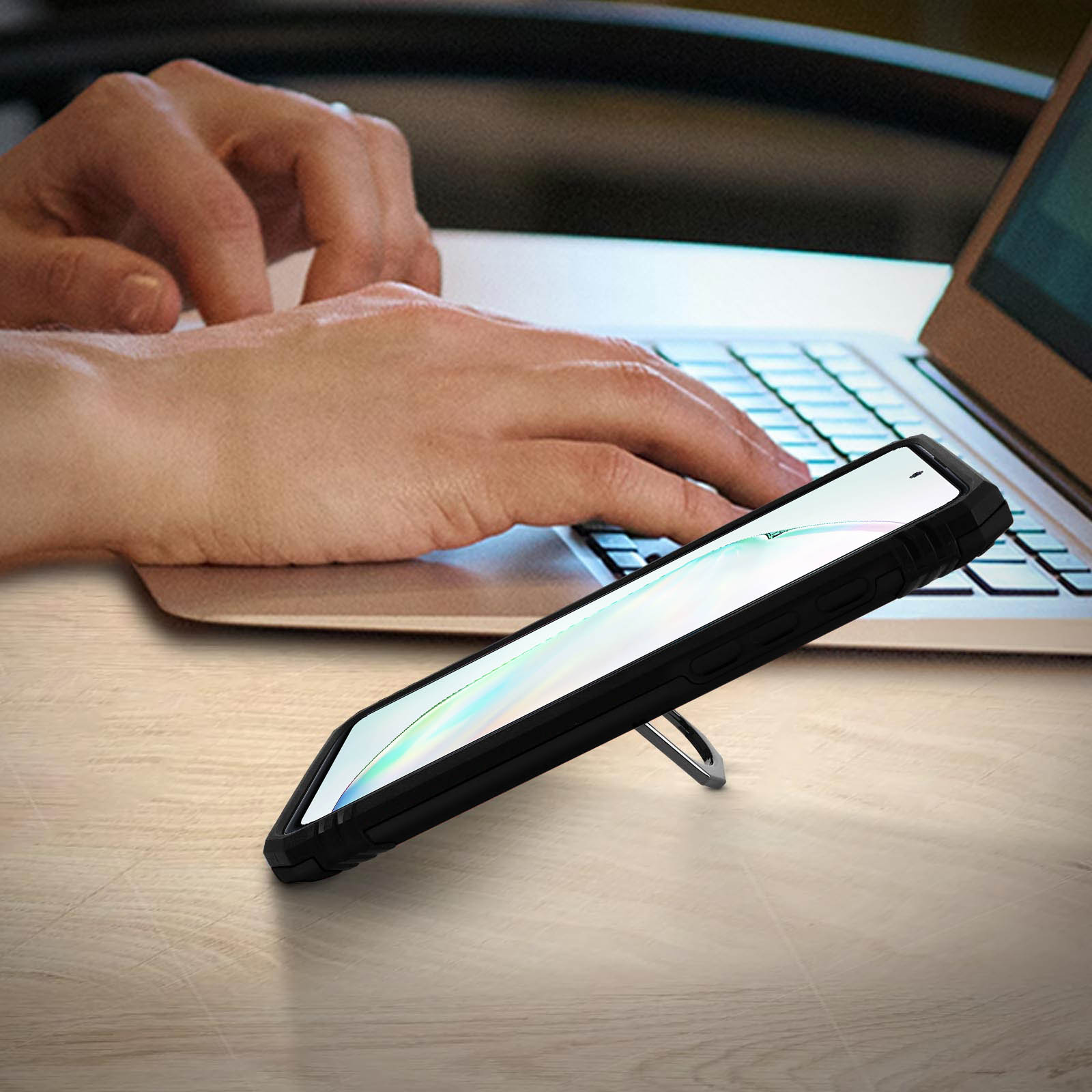 Mano che usa un laptop. Telefono sul tavolo con supporto. Telefono con custodia. Sfondo sfocato.