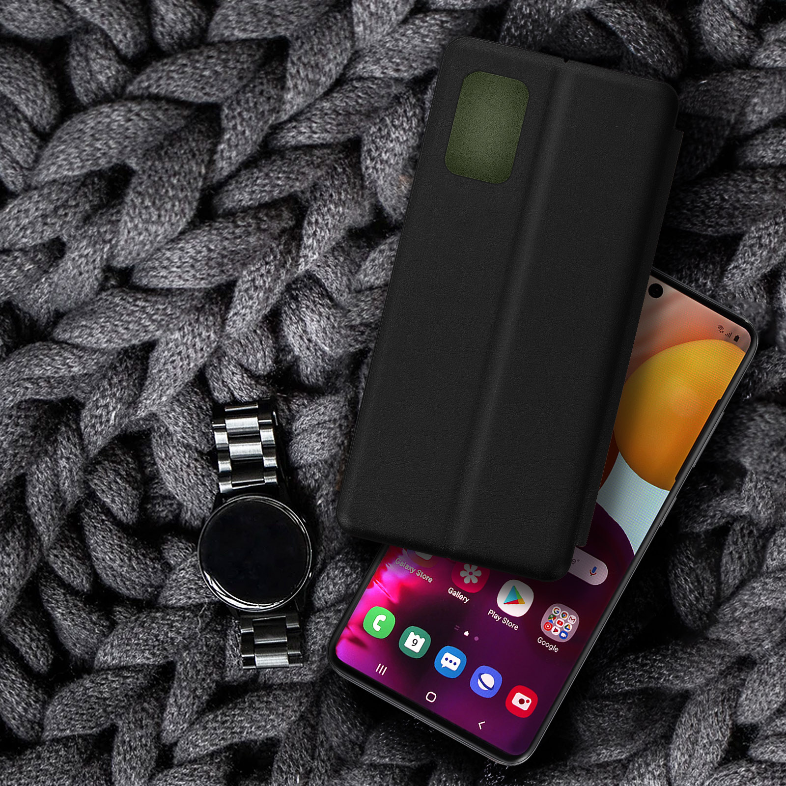 Telefon mit Hülle und Uhr auf grauer Strickdecke.