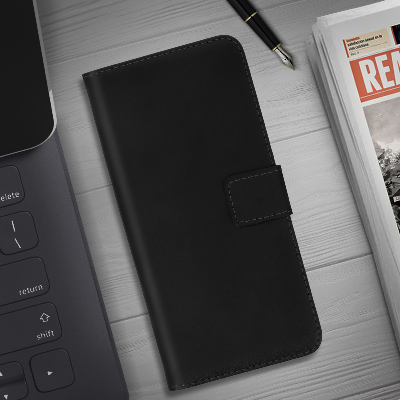 Étui de téléphone noir sur une table blanche avec un ordinateur portable, un stylo et un journal. L'étui est fermé.