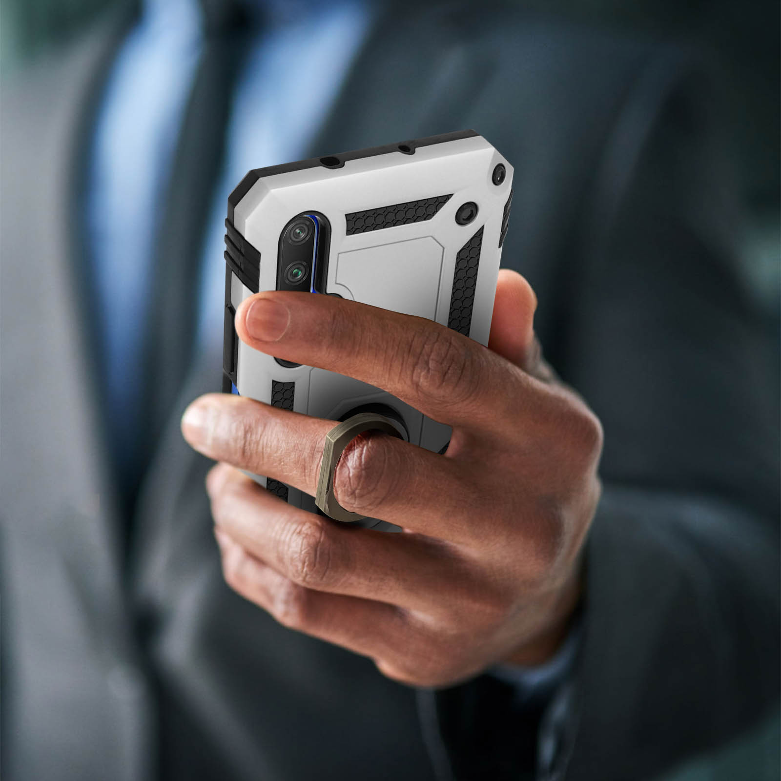 Persona che tiene in mano un telefono con una custodia bianca e grigia, un anello al dito.