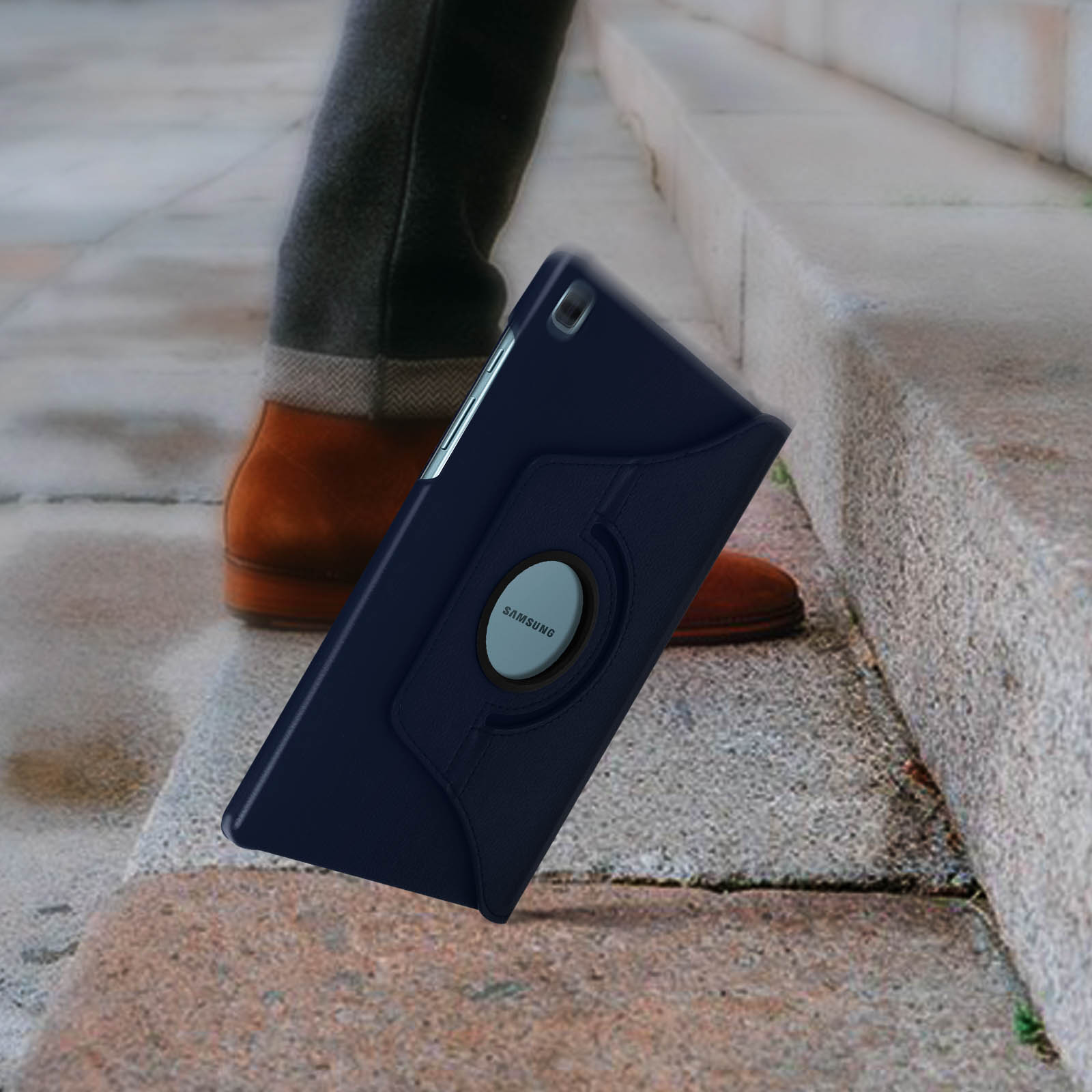 Tablet con custodia blu, tenuto da una persona che cammina sulle scale. Scarpe marroni visibili.