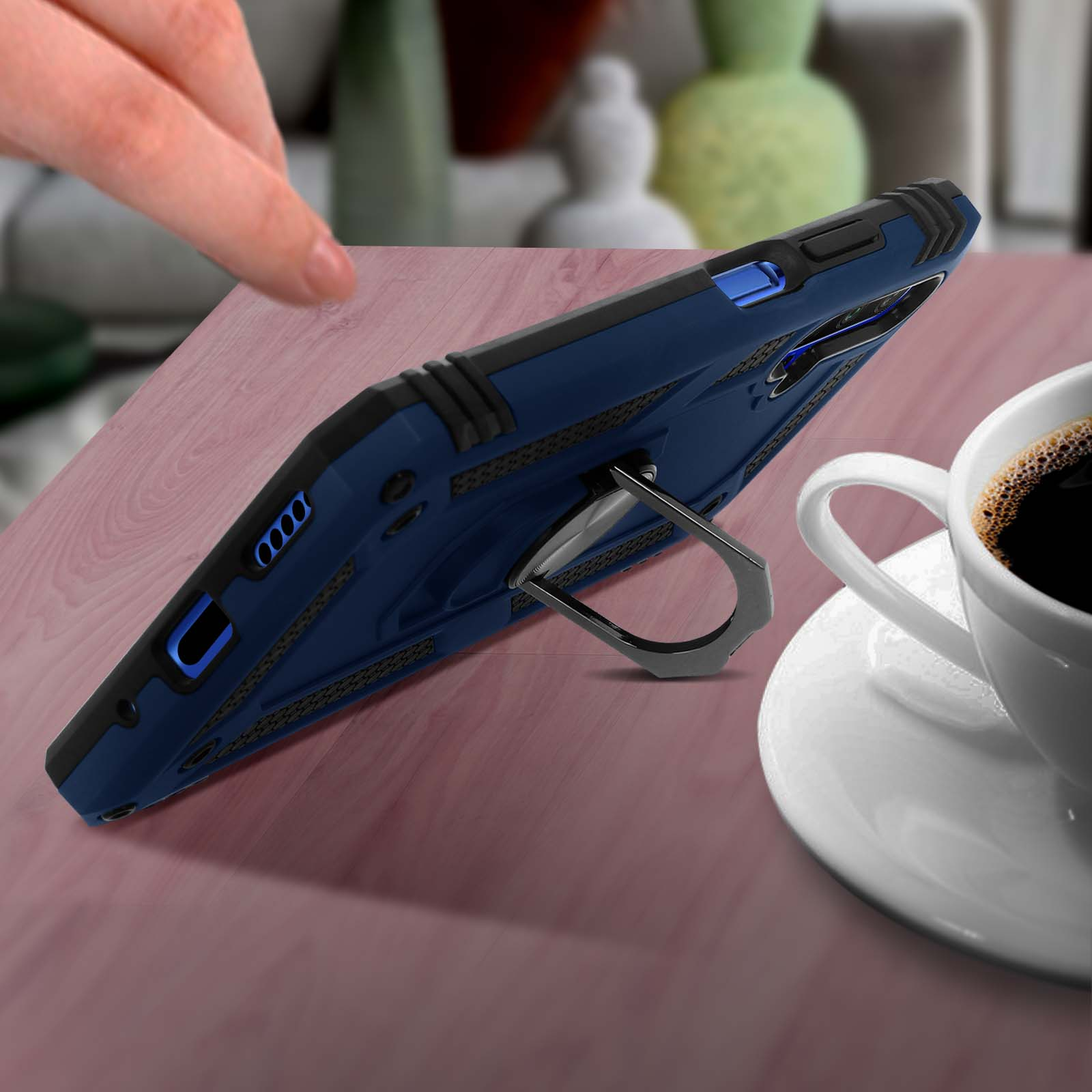 Coque de téléphone bleue avec support annulaire sur une table, tasse à café à droite. Main en haut.