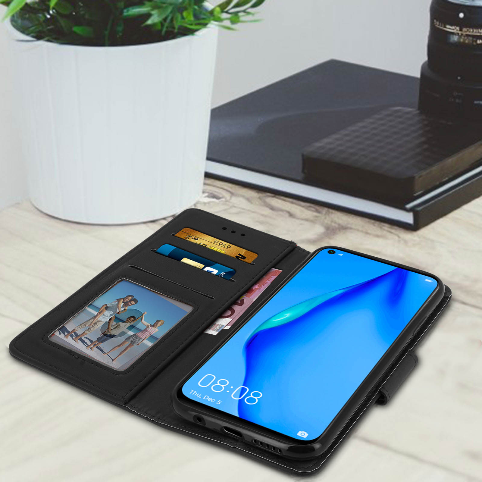 Custodia nera con telefono, carte e denaro aperti su tavolo di legno.