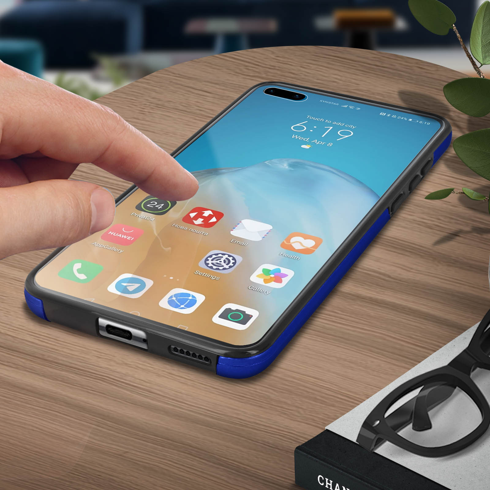 Mano che tocca lo schermo del telefono mostrando icone delle app. Telefono in custodia blu e nera sul tavolo.