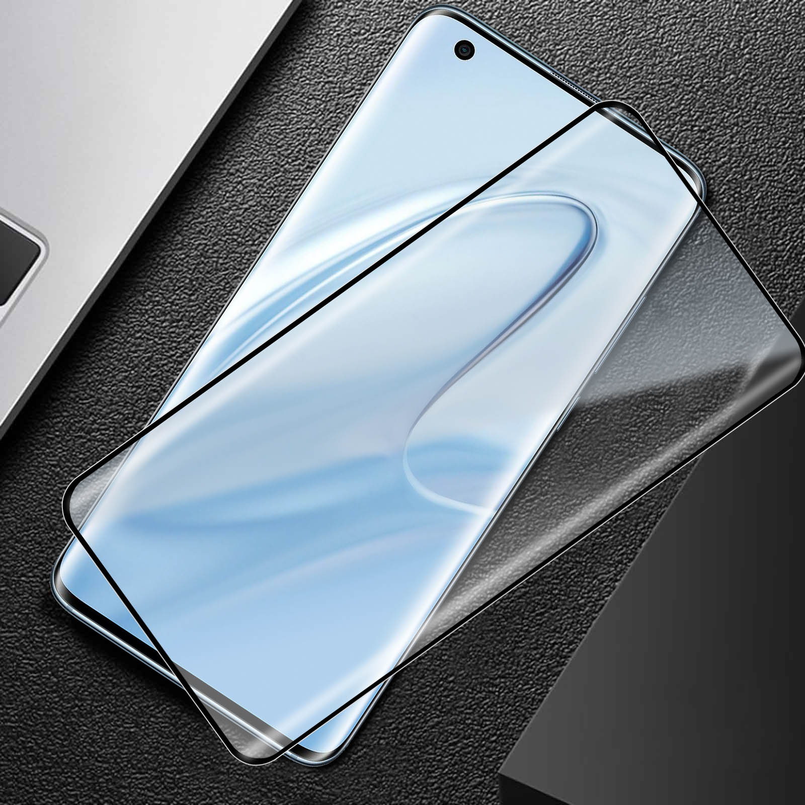 Uno schermo curvo di smartphone coperto da una protezione, su una superficie nera strutturata.