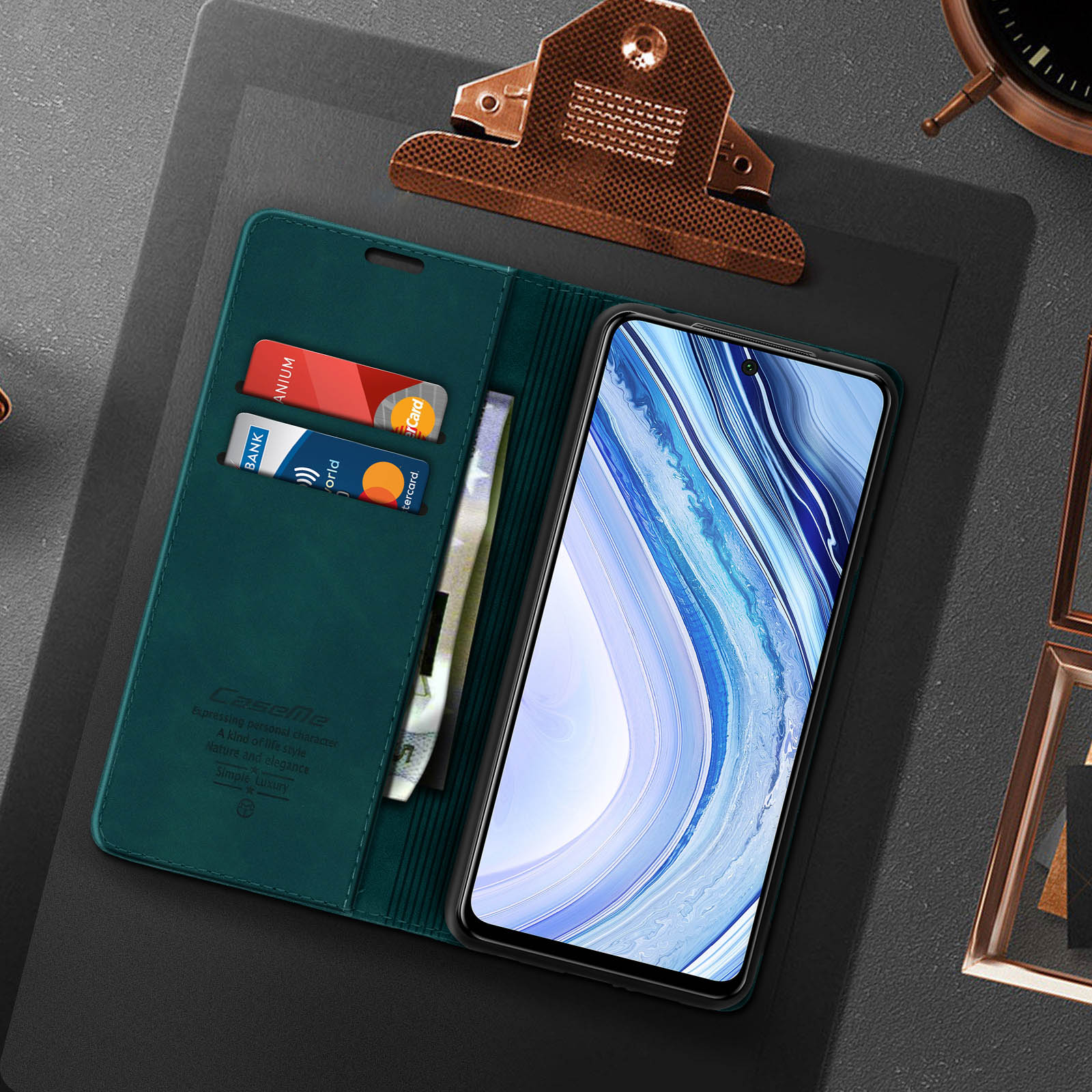 Custodia verde con carte e denaro, telefono accanto. Clip metallico e orologio su superficie scura.