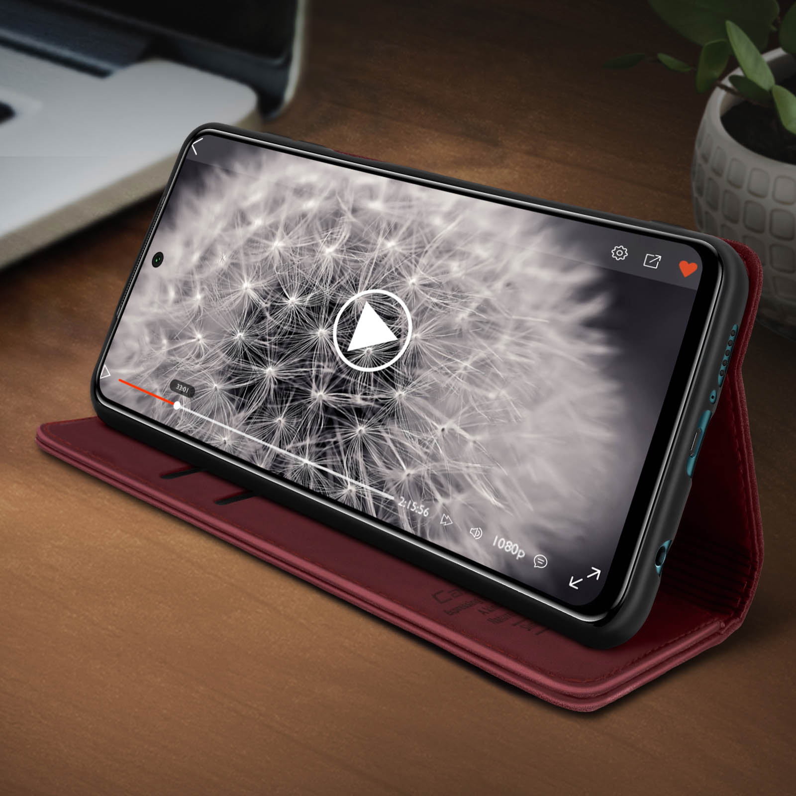 Telefono su supporto rosso, mostra un video. Tavolo in legno, sfondo sfocato.