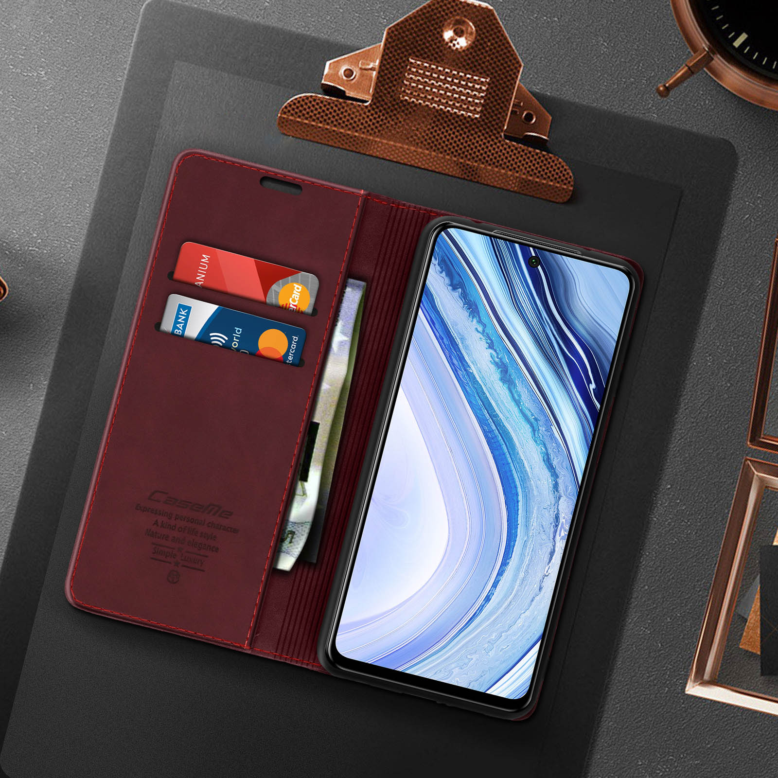 Custodia del telefono aperta, che mostra carte e denaro. Telefono a destra. Scrivania con altri oggetti.