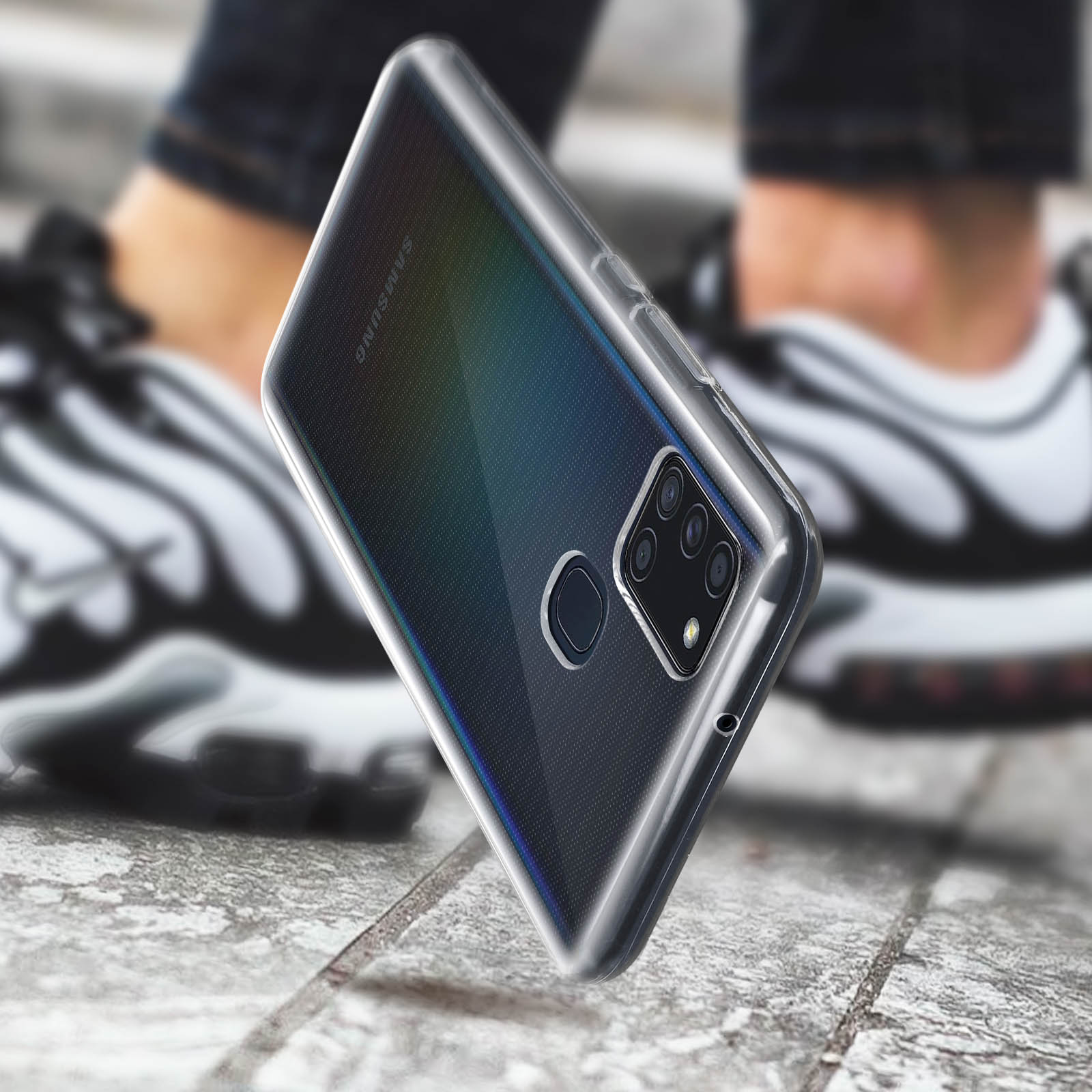 Custodia trasparente su un telefono. Gambe e scarpe di una persona sullo sfondo.