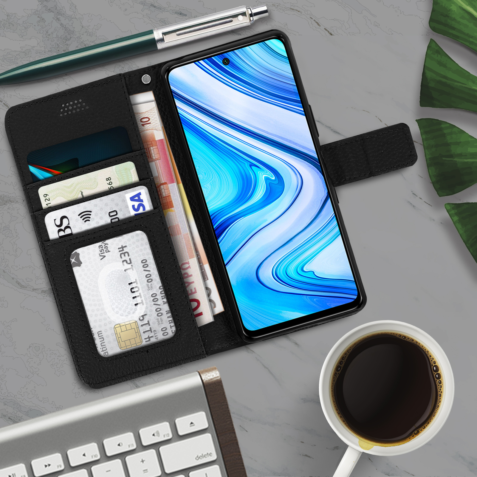 Een telefoon met kaarten, geld, een pen en een kop koffie op een marmeren oppervlak, met een toetsenbord.