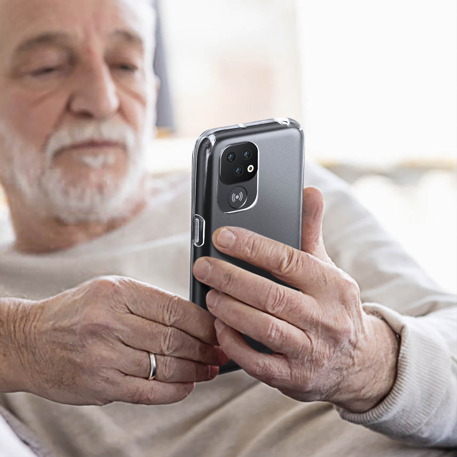 Un uomo anziano tiene un telefono con una custodia trasparente. È seduto, sfondo sfocato.