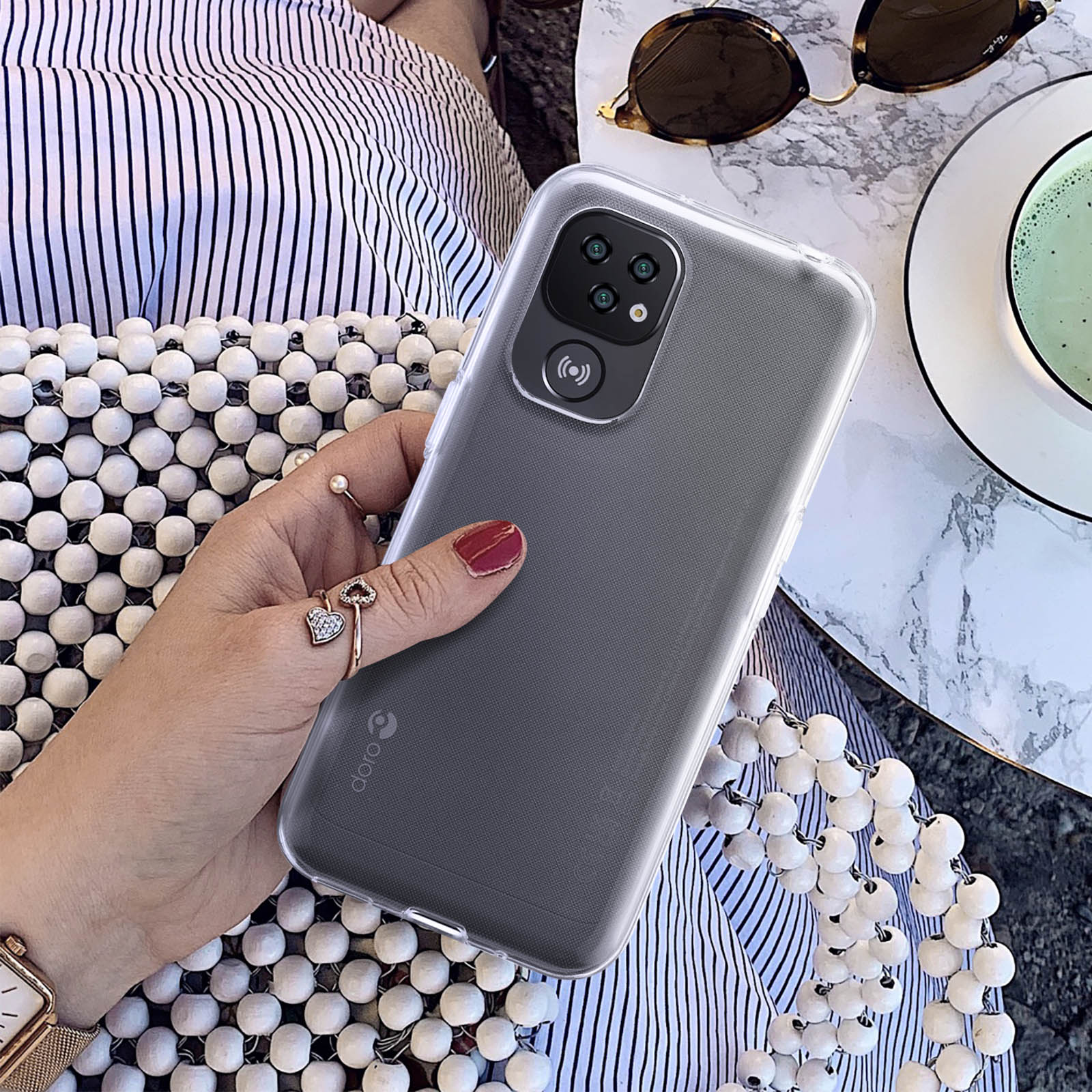 Una mano tiene in mano un telefono con una custodia trasparente. Il telefono ha una tripla fotocamera sul retro.