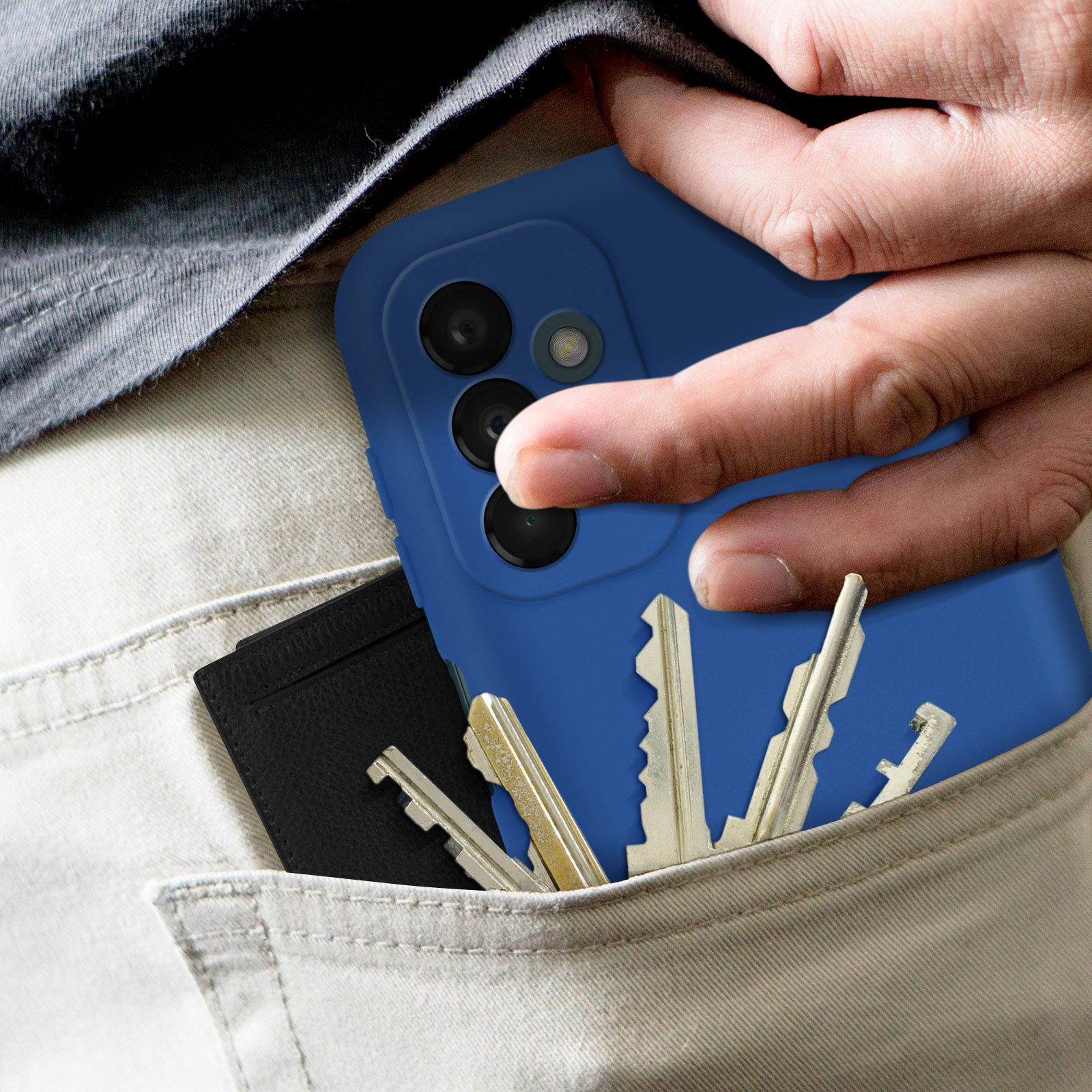 Mano che tiene un telefono blu. La tasca ha chiavi e un porta carte nero. Pantaloni colorati chiari.